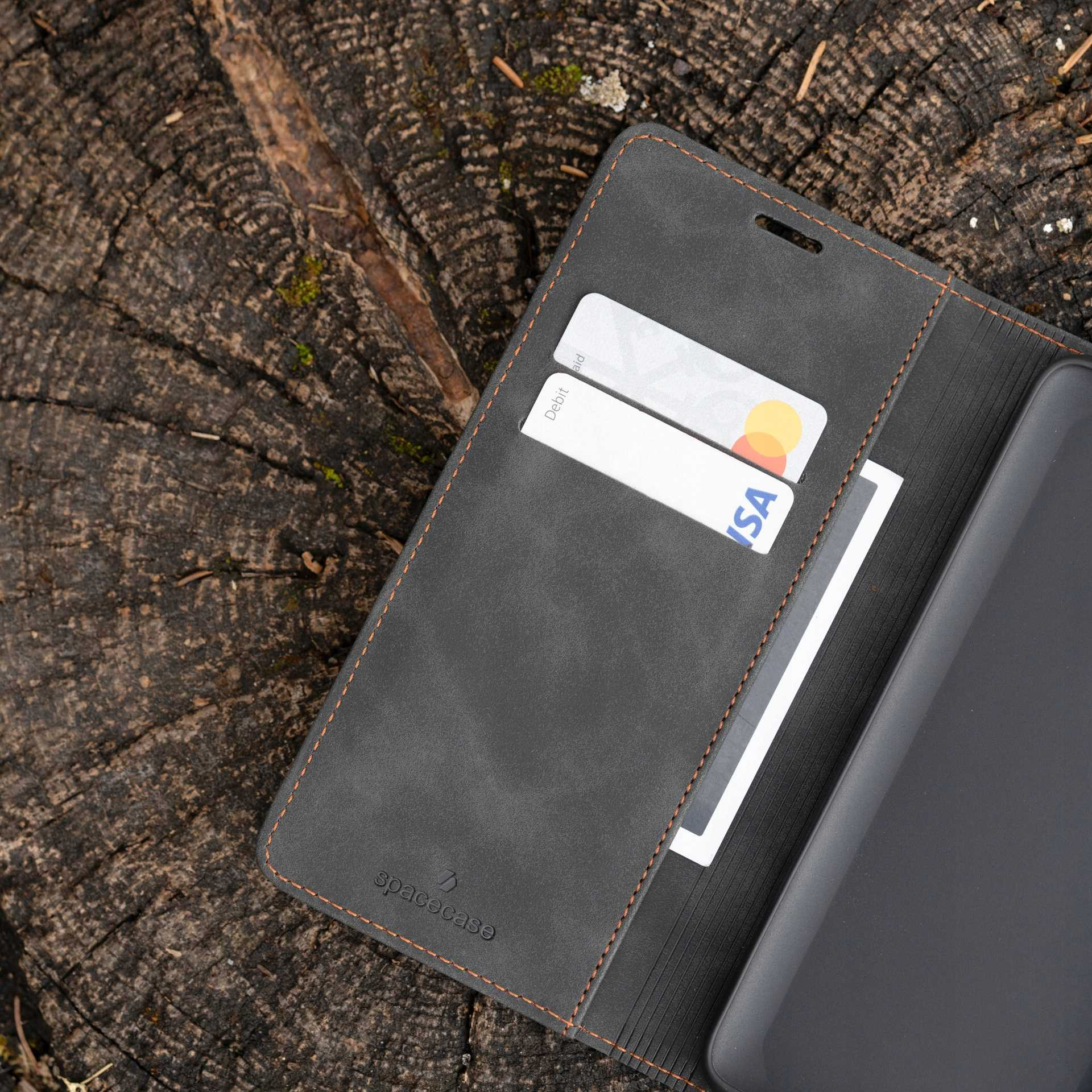 Ciemnoszare etui na telefon z kartami, na drewnie, ze szwami.