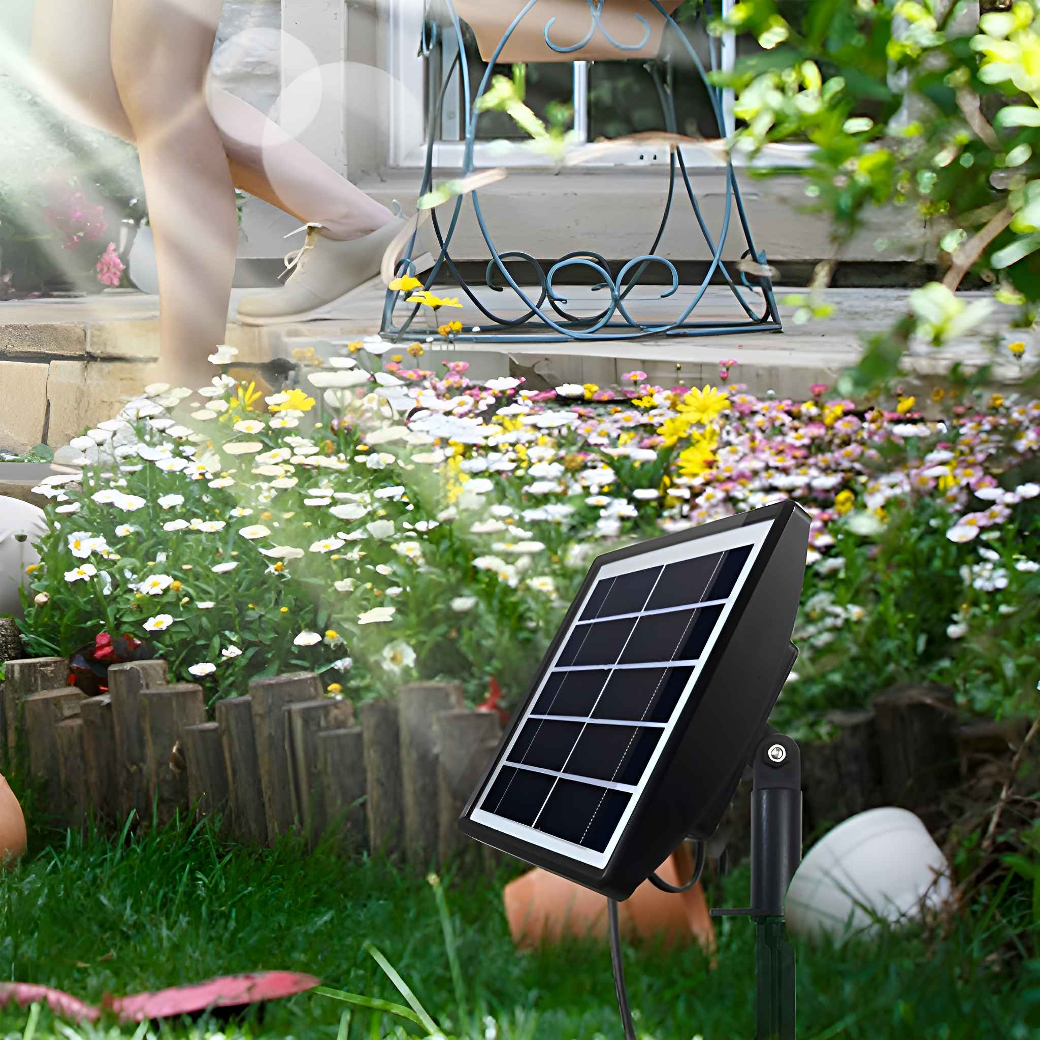 Ein kleines Solarpanel in einem Garten mit Blumen und Beinen einer Person.