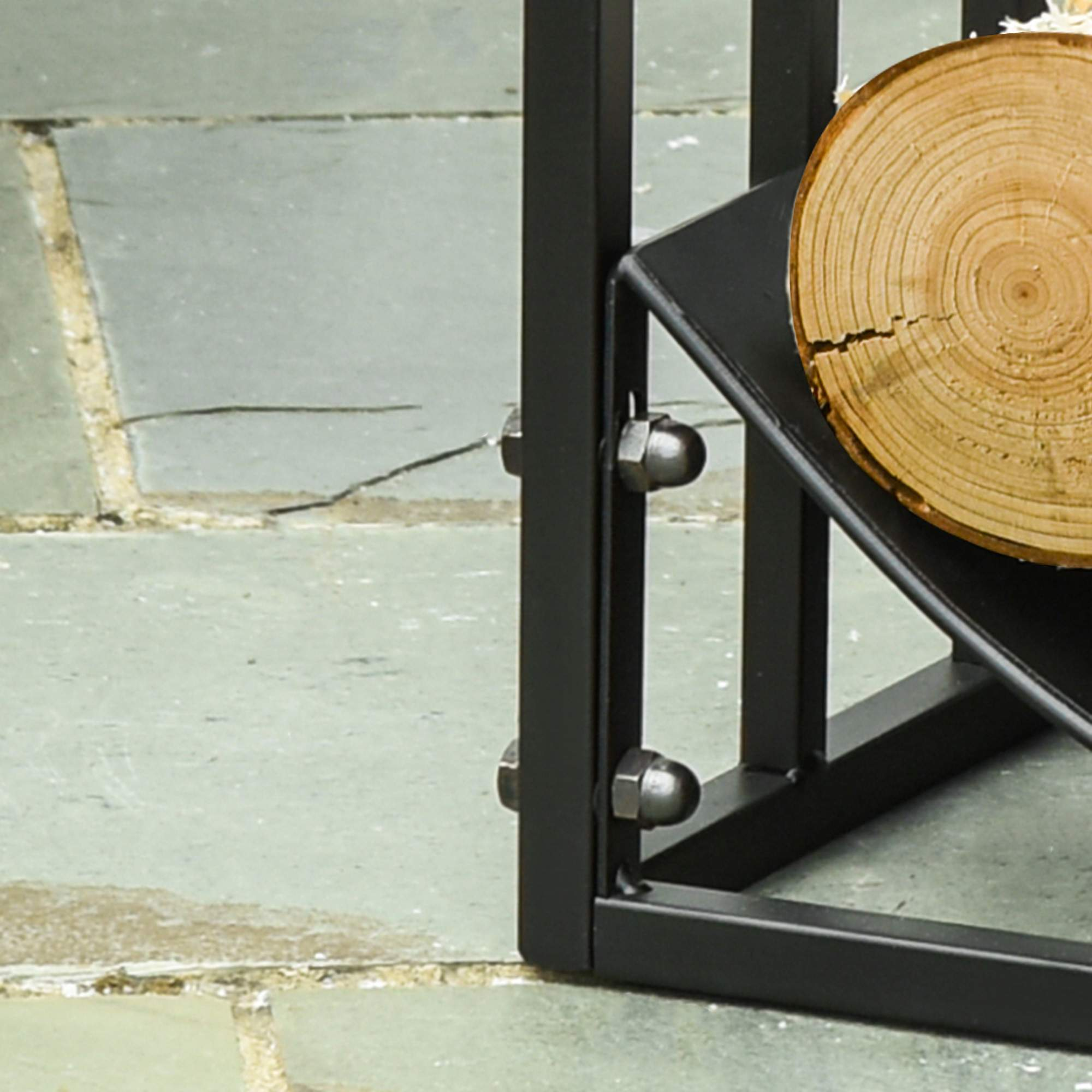 Nahaufnahme einer schwarzen Metallecke eines Holzhalters. Ein Baumstamm und Bolzen sind sichtbar. Grauer Steinboden darunter.