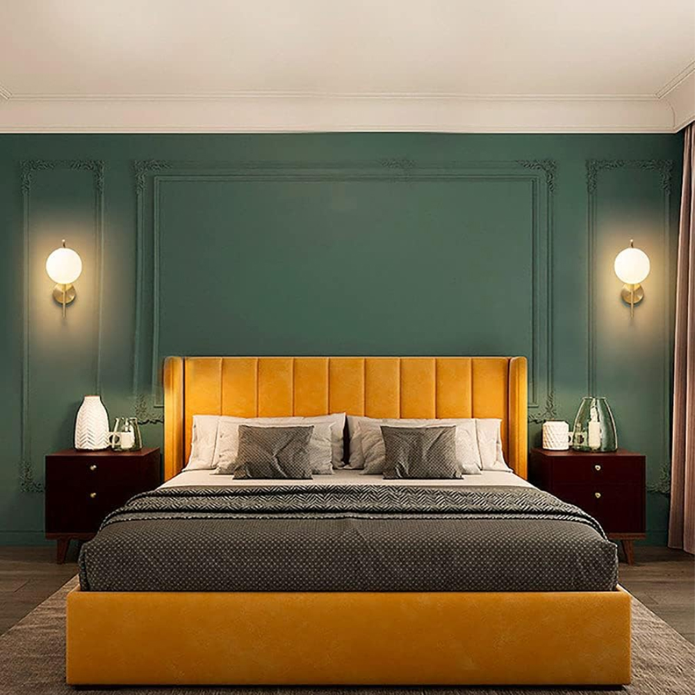 Ein Schlafzimmer mit gelbem Bett, grüner Wand und zwei Nachttischen. Zwei Lampen sind an der Wand.