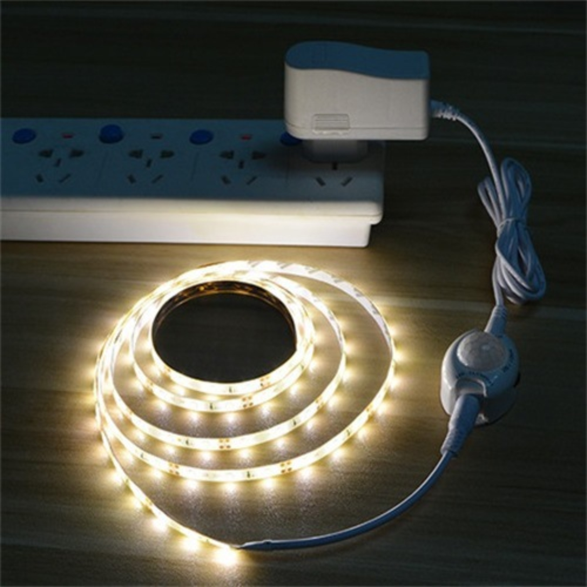 Eine leuchtende LED-Leiste, die sich in der Nähe einer Steckdose mit angeschlossenem Adapter befindet.