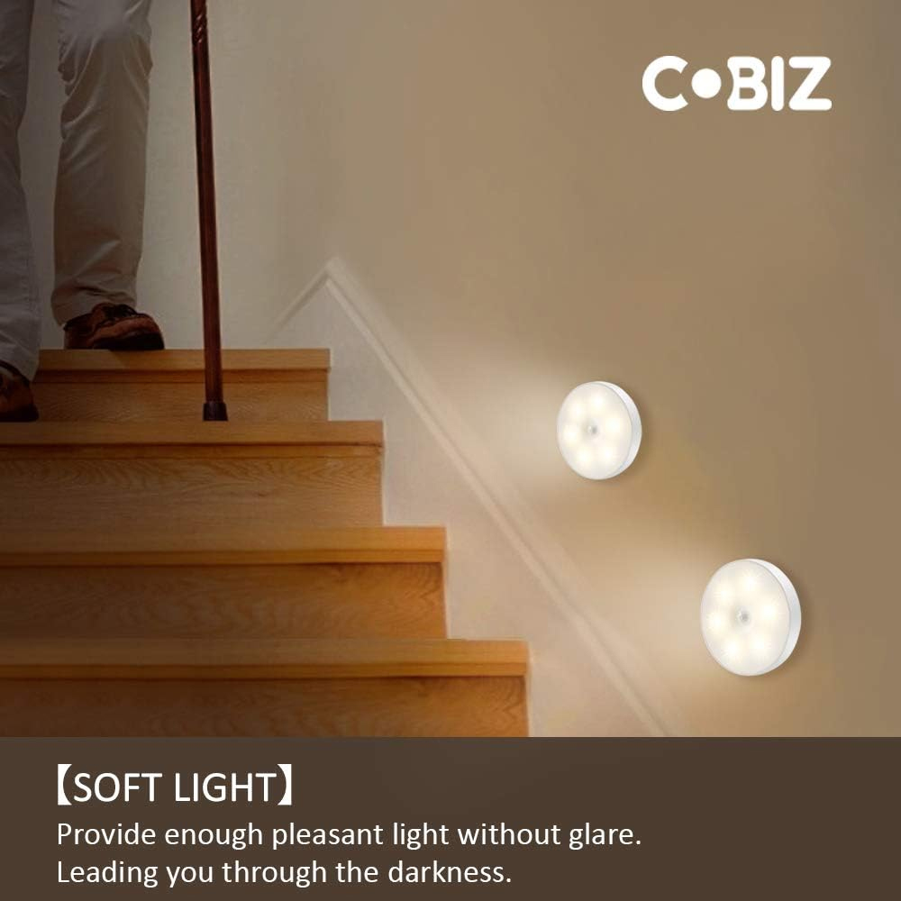 Zwei weiße LED-Leuchten an einer Wand, mit einer Person, die eine Holztreppe hinaufgeht.