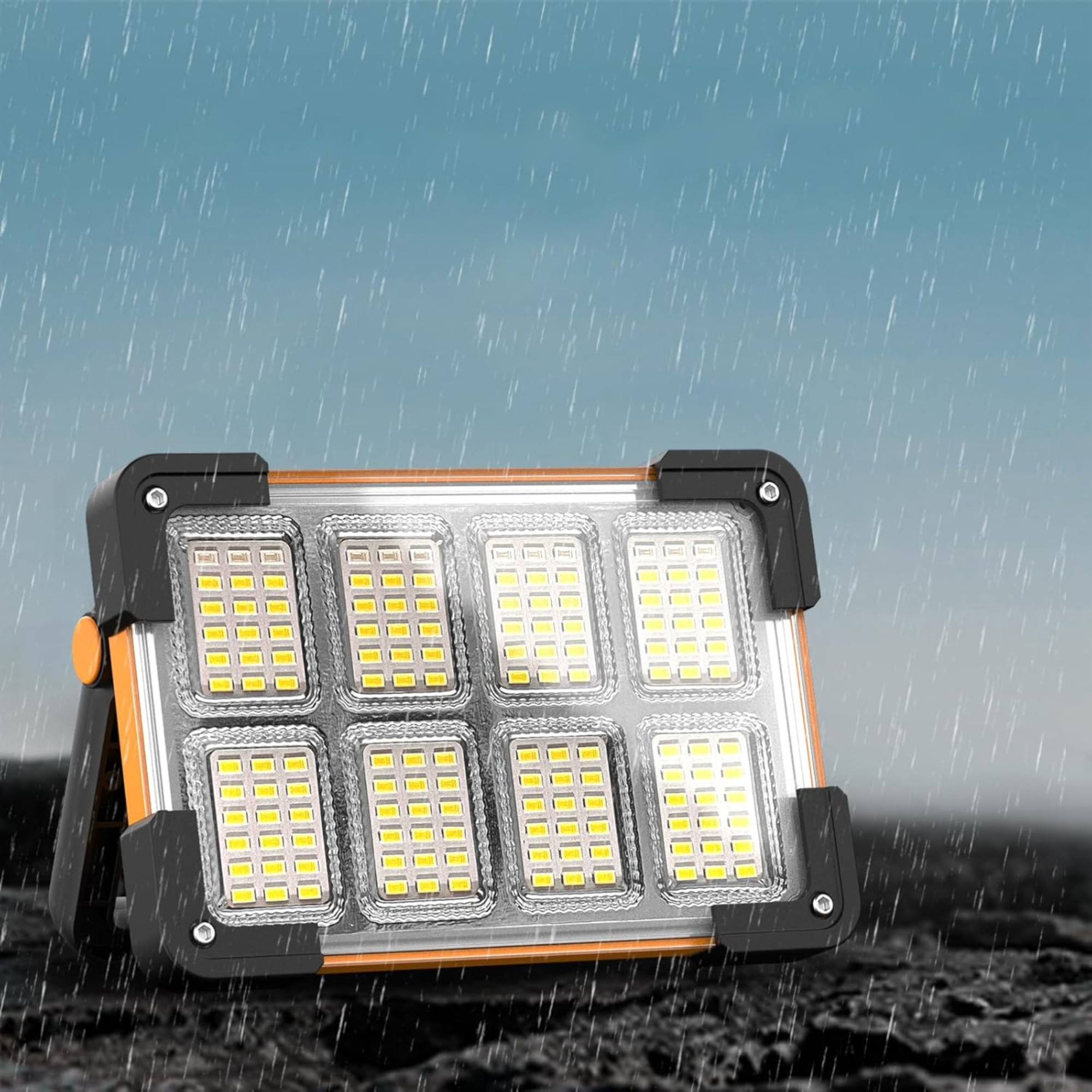 Ein heller LED-Flutlichtstrahler, orangefarbener und schwarzer Rahmen, mit Regen und dunklem Hintergrund.
