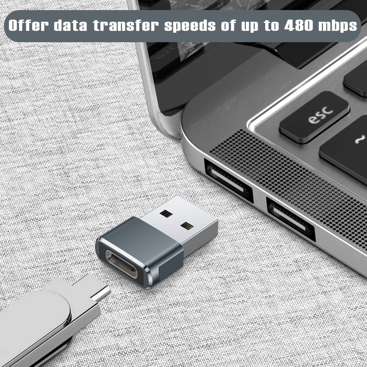 Ein USB-C-Adapter neben einem Laptop. Der Adapter ist silberfarben und hat einen USB-Anschluss.