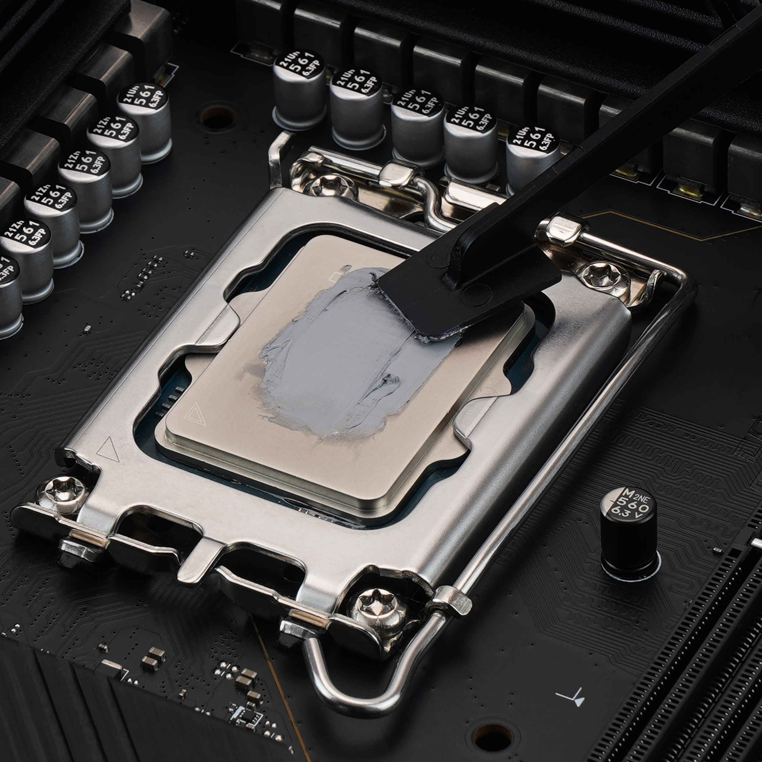 Eine CPU wird mit einem kleinen schwarzen Werkzeug mit Wärmeleitpaste auf einem schwarzen Motherboard bestrichen.