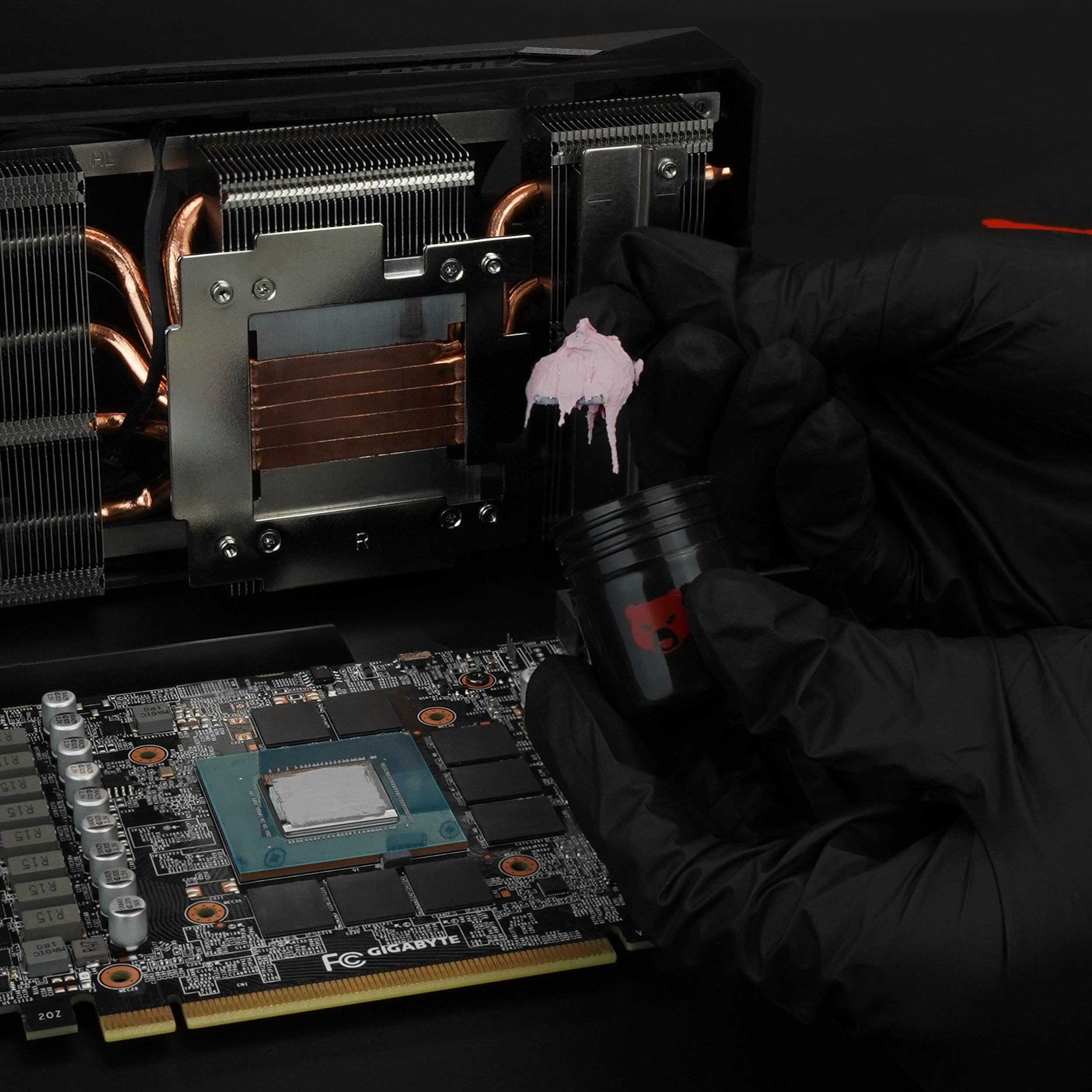 Eine Person trägt Wärmeleitpaste auf eine Computerkomponente auf. Schwarze Handschuhe, ein schwarzer Behälter.