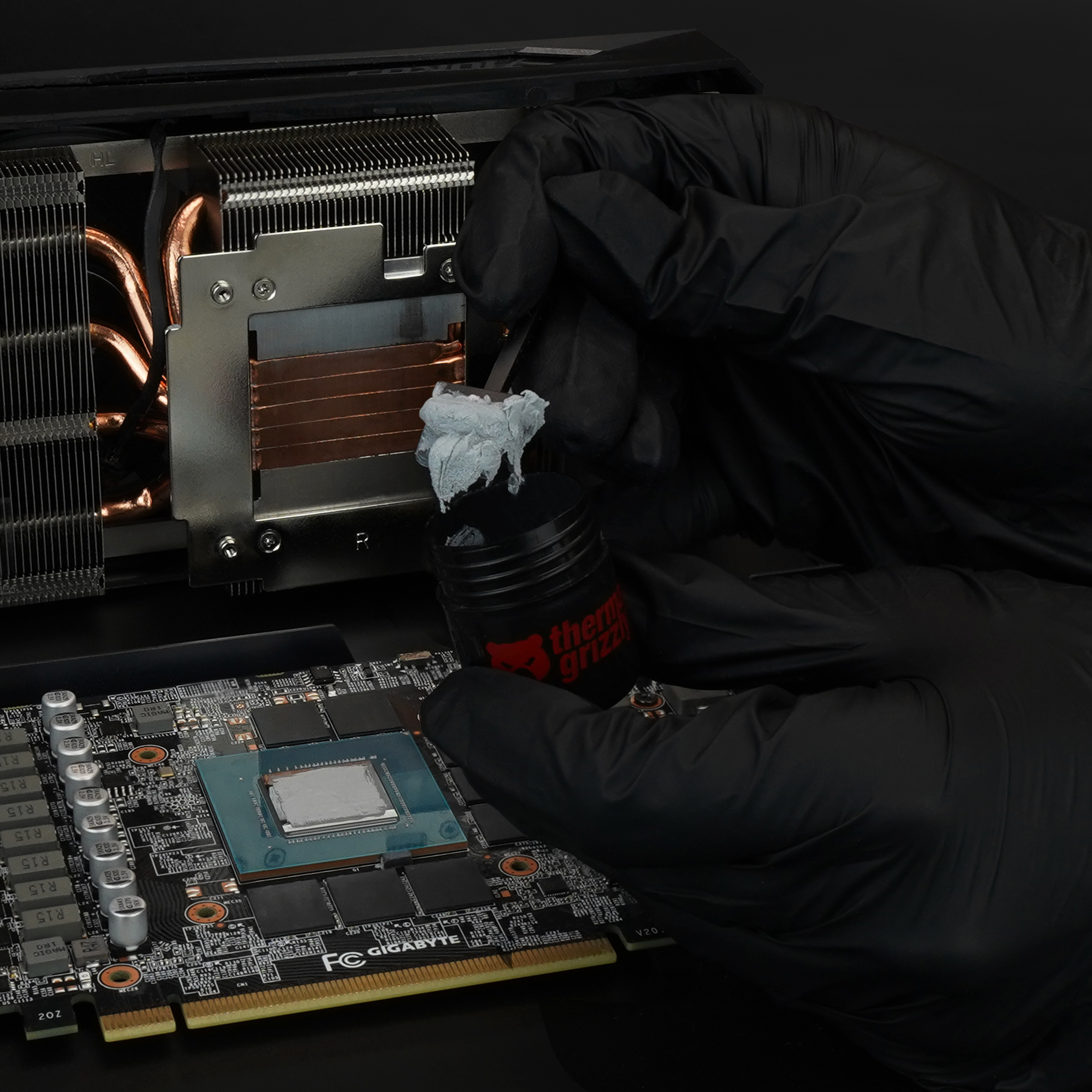 Hände mit schwarzen Handschuhen, die Wärmeleitpaste auf eine Computerkomponente auftragen.