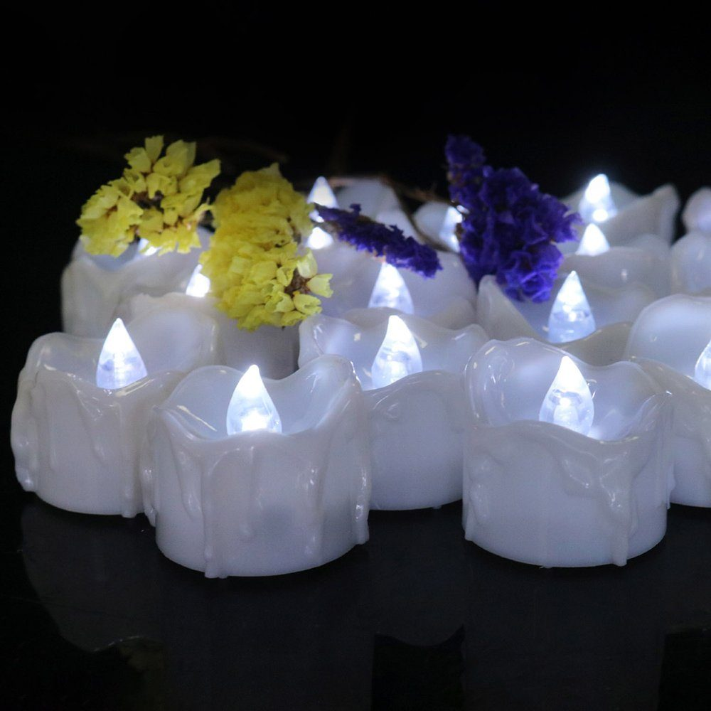 Weiße LED-Kerzen mit gelben und lila Blüten auf der Oberseite. Die Kerzen stehen auf dunklem Untergrund.