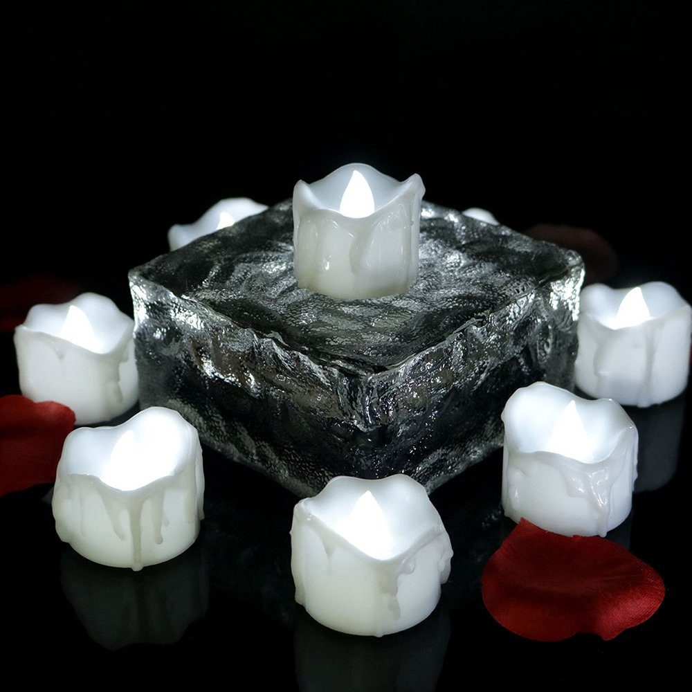 Weiße Kerzenlichter auf einer Glasoberfläche mit roten Rosenblättern. Die Kerzen sind in Blockformation.