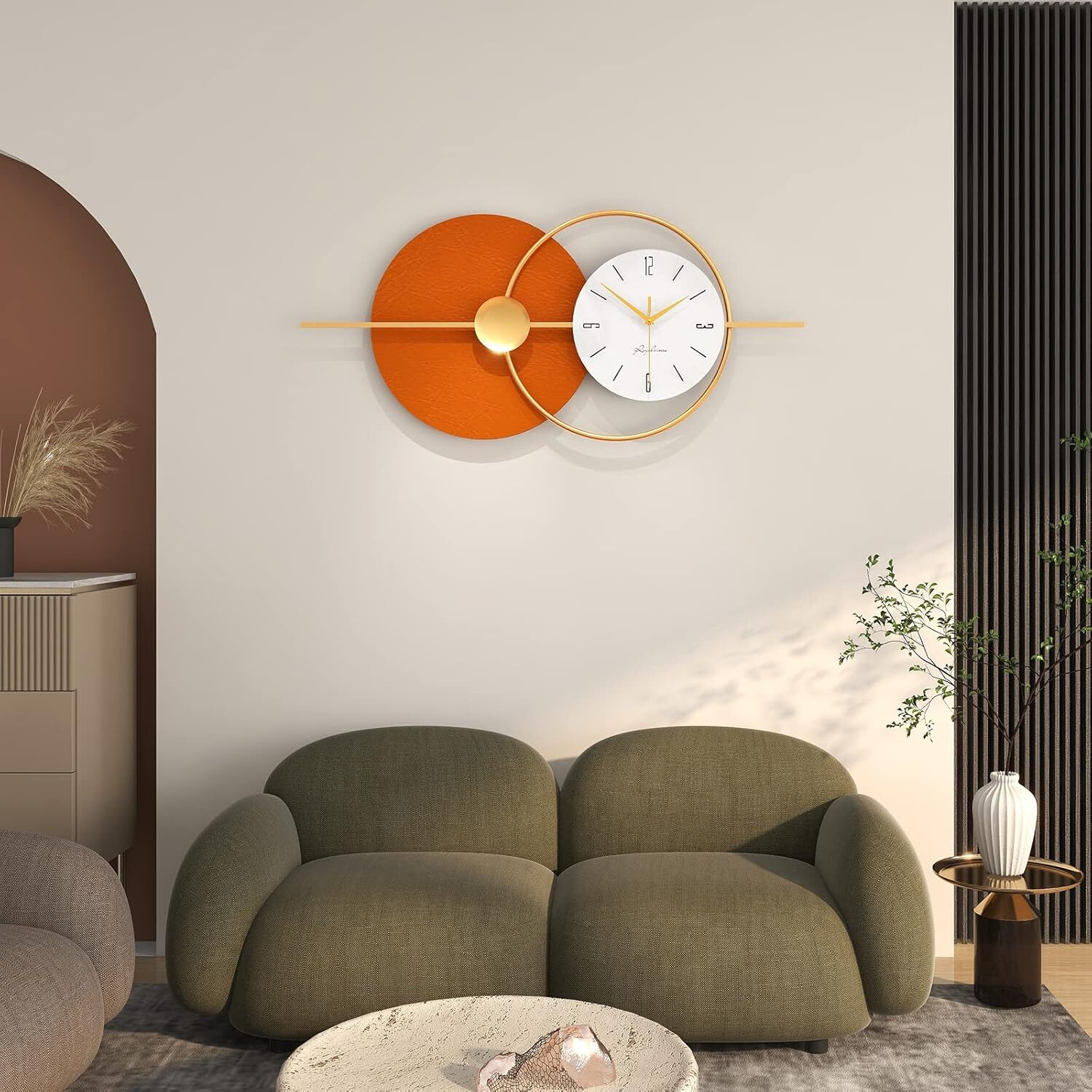 Eine Uhr an der Wand mit einem orangefarbenen Kreis und einem weißen Zifferblatt. Darunter ein Sofa.