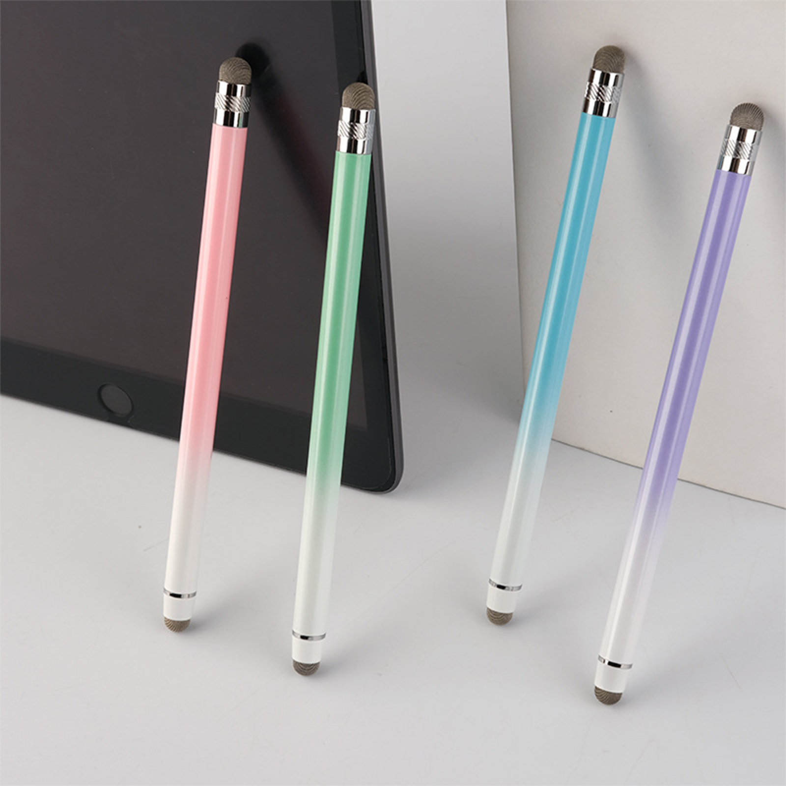 Vier Stifte mit Farbverlauf, die auf einem Tisch neben einem Tablet liegen.