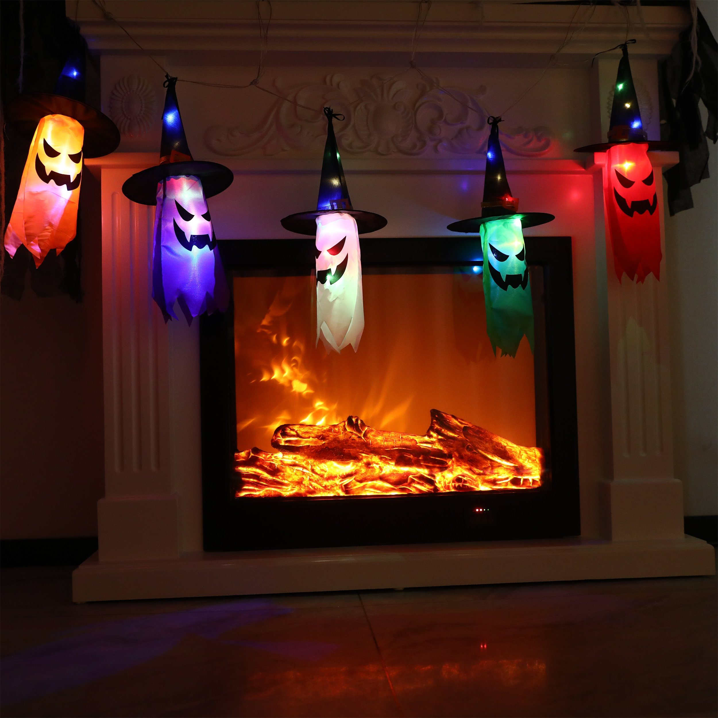 Halloween-Geisterdekorationen mit Hexenhüten vor einem Kamin, beleuchtet.