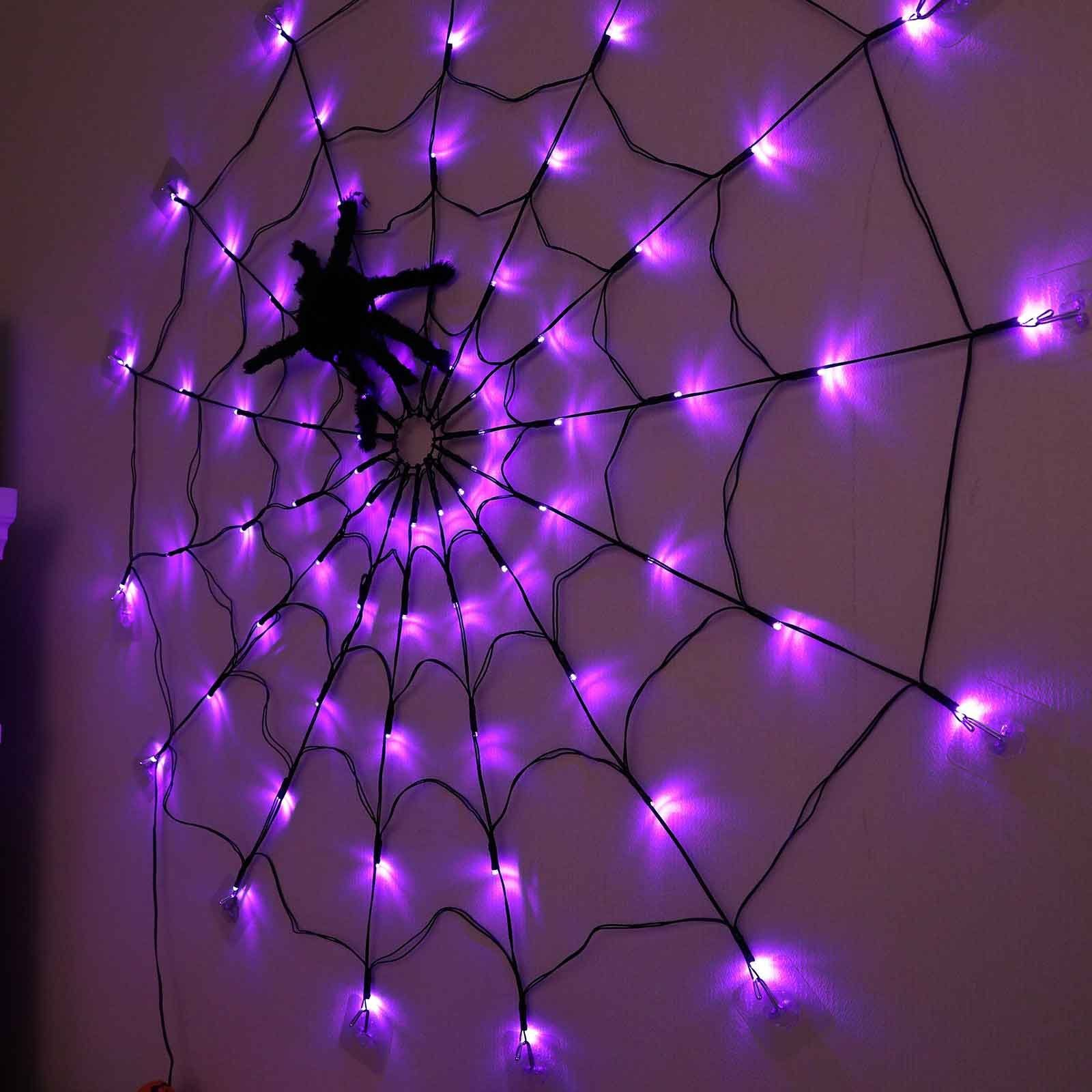 Ein lila Spinnennetz mit einer schwarzen Spinne in der Mitte. Beleuchtet mit vielen kleinen lila Lichtern. An einer Wand.