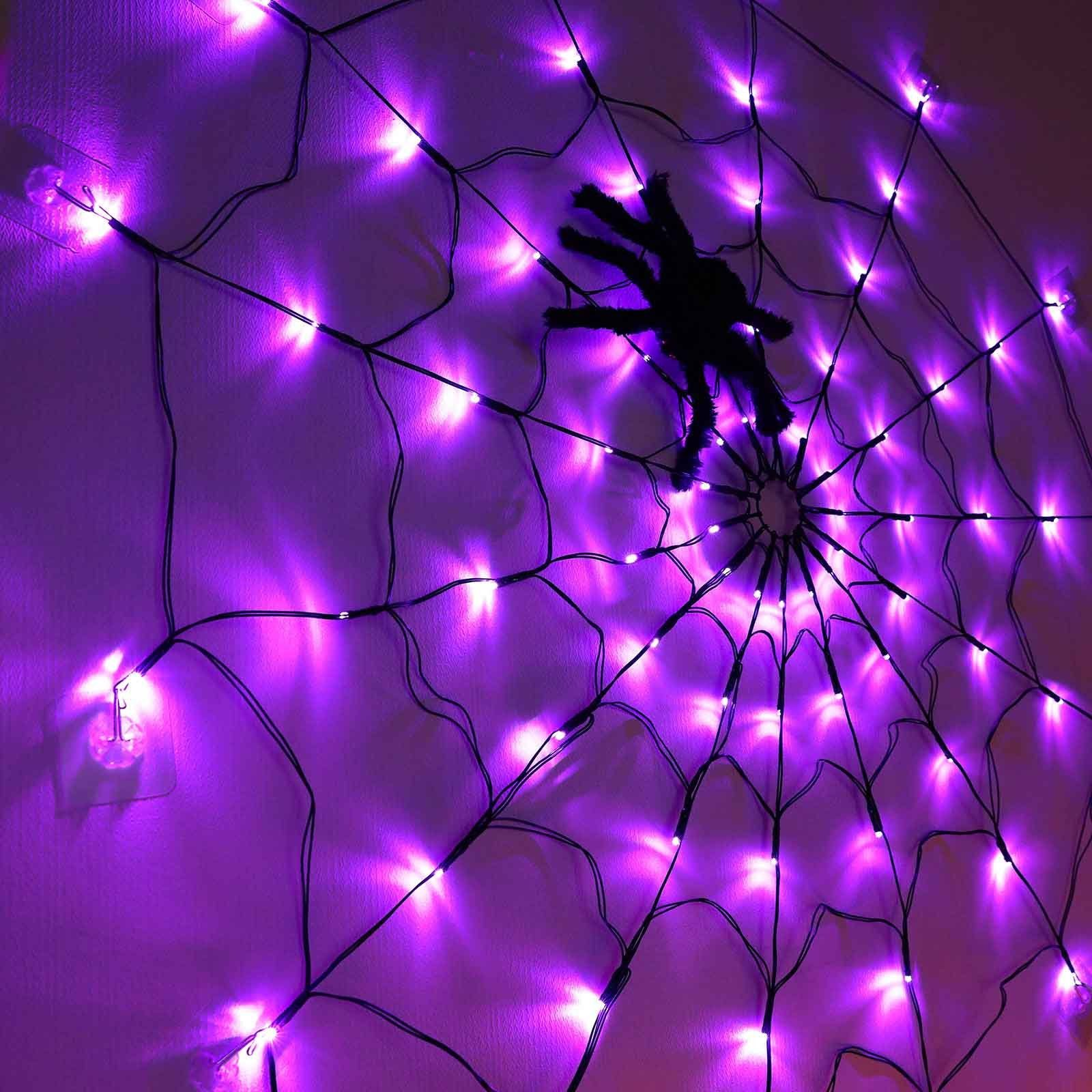 Nahaufnahme eines lila Spinnennetzes mit einer schwarzen Spinne. Das Netz ist mit lila Lichtern an der Wand beleuchtet.