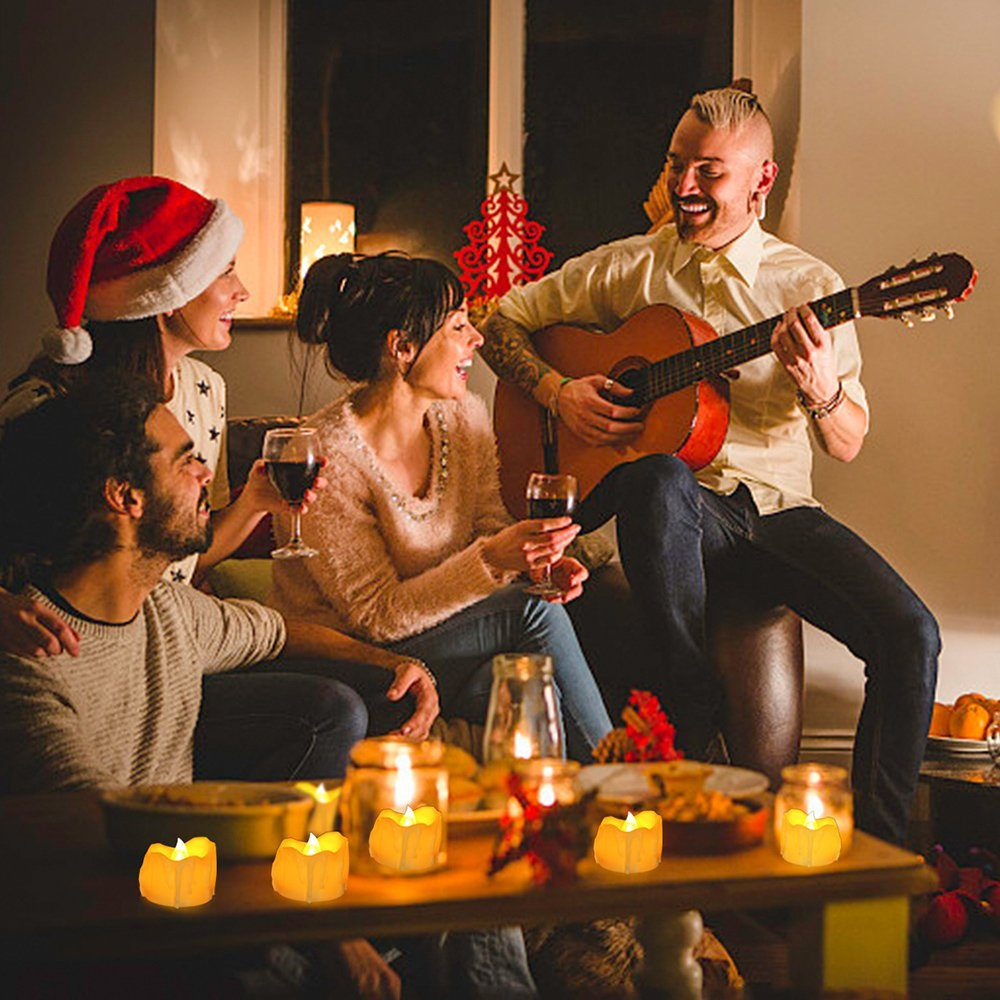 Eine Gruppe von Leuten sitzt an einem Tisch mit Kerzen und Wein. Ein Mann spielt Gitarre.