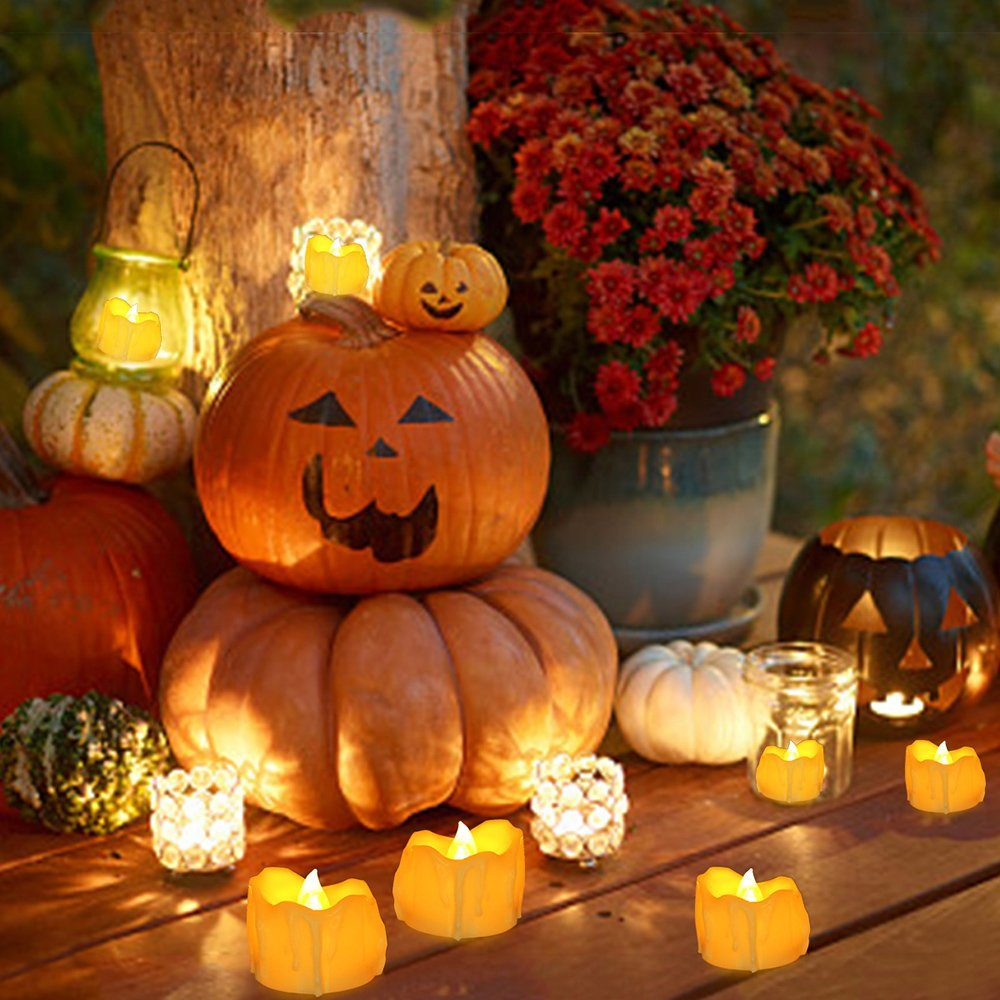 Halloween-Dekorationen auf einem Holztisch, darunter Kürbisse, Kerzen und Blumen.