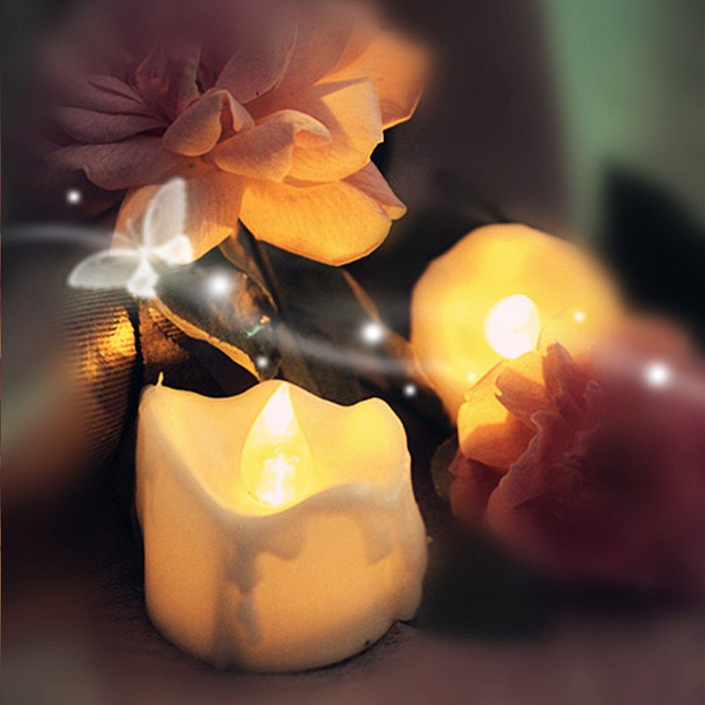 Nahaufnahme einer Kerze mit Flamme, umgeben von Blumen. Weiche Beleuchtung und verschwommener Hintergrund.