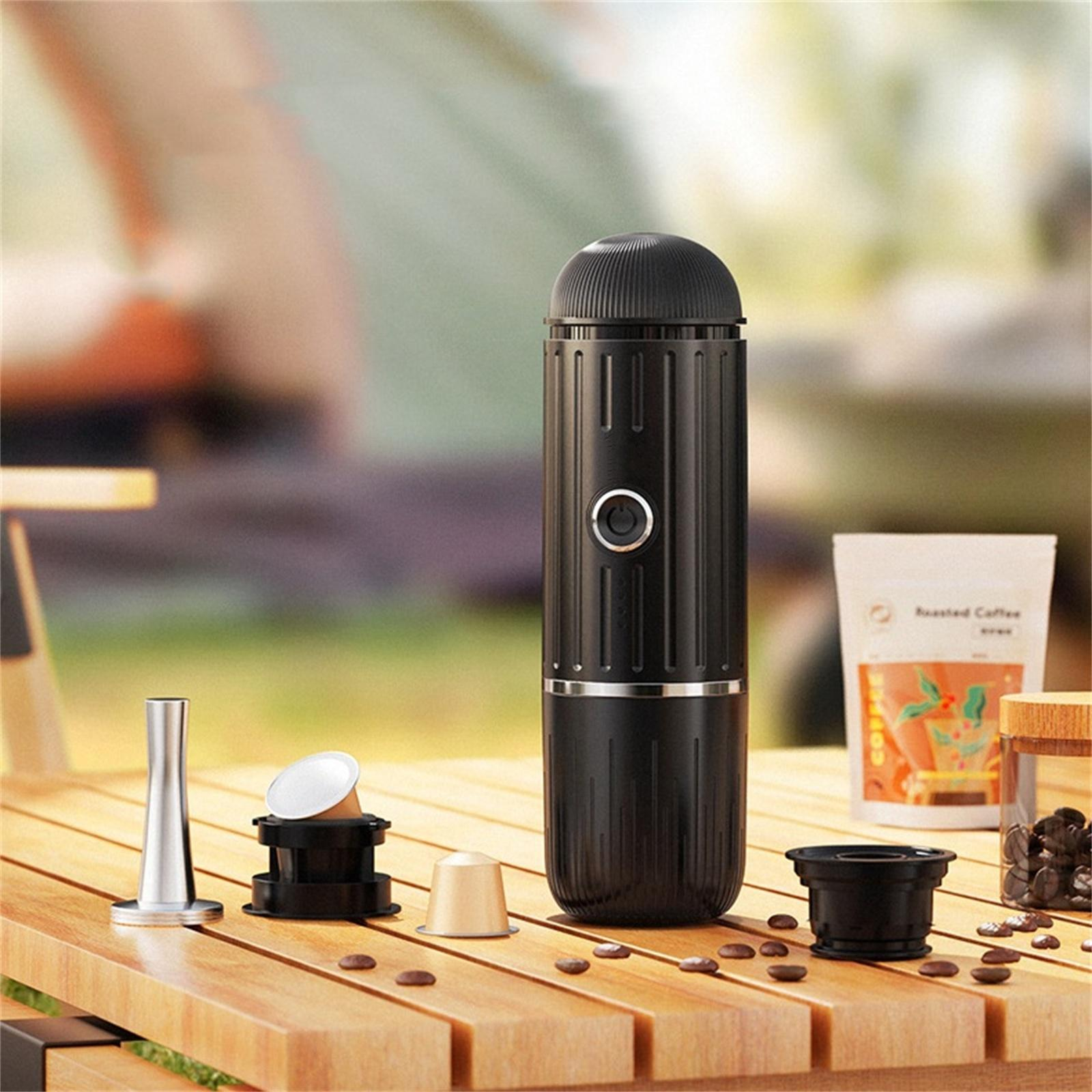 Eine schwarze tragbare Kaffeemaschine mit Zubehör auf einem Holztisch. Kaffeebohnen und ein Kaffeebeutel.