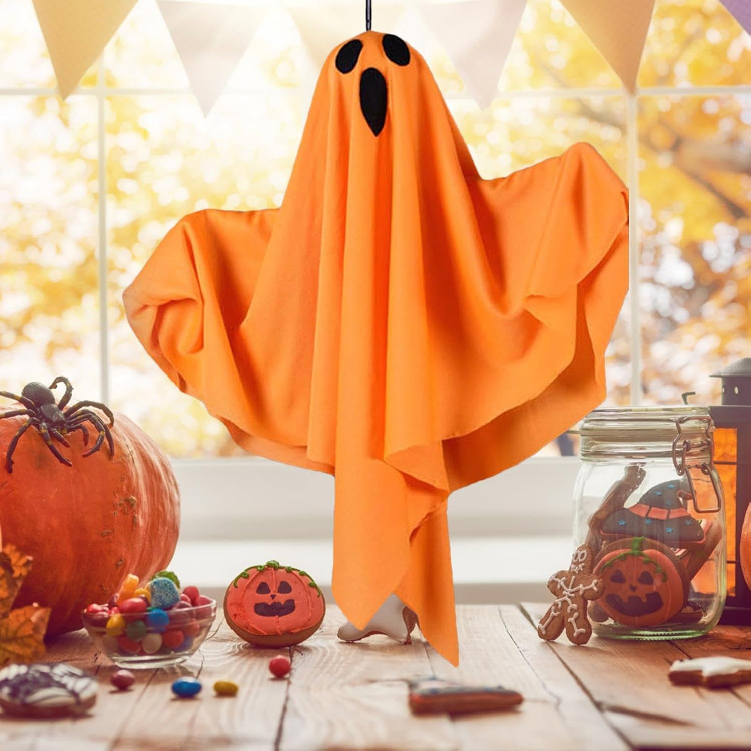 Orange Geisterdekoration mit schwarzen Augen und breitem Mund. Halloween-Szene mit Kürbissen und Süßigkeiten.