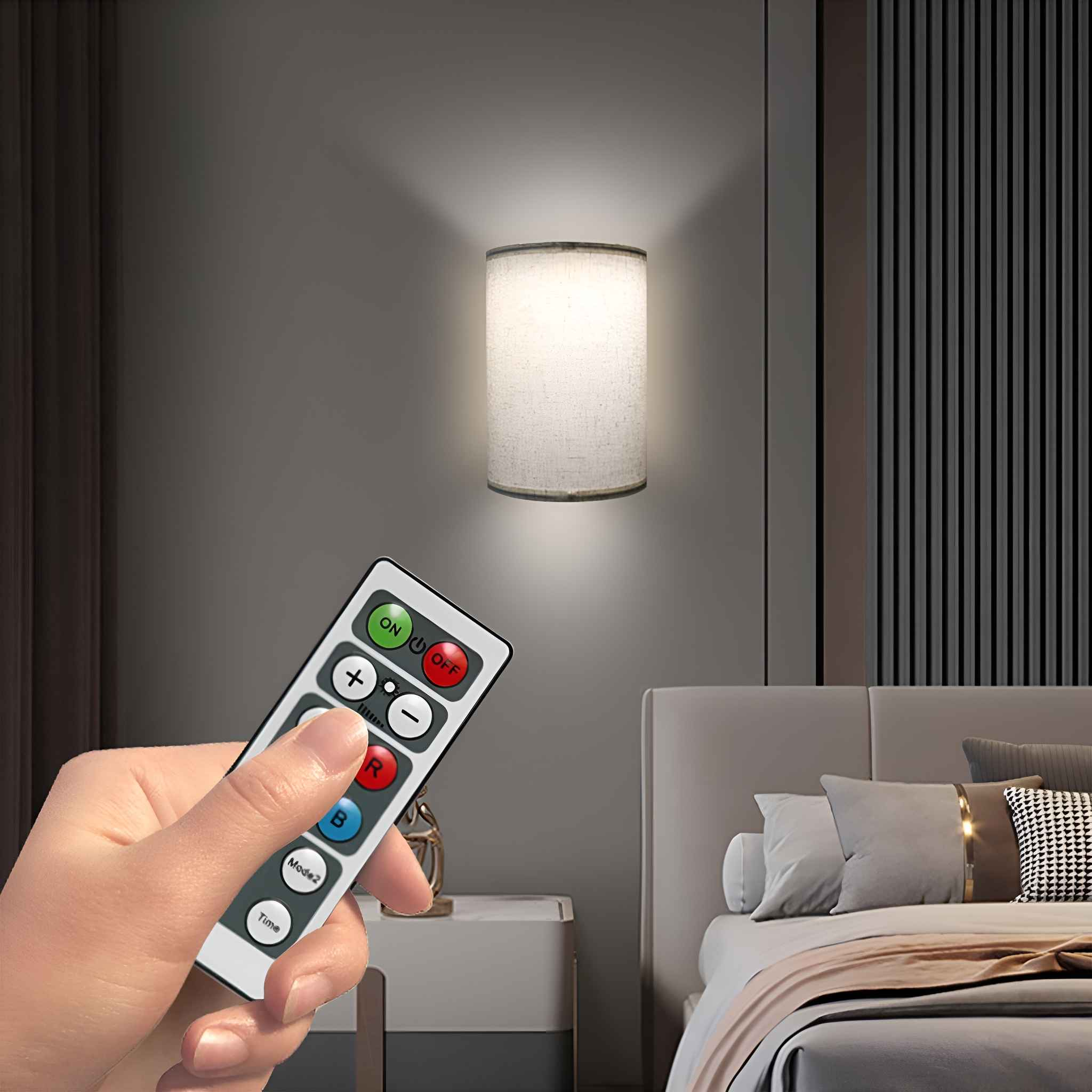 Hand hält Fernbedienung, steuert eine Wandlampe über einem Bett.