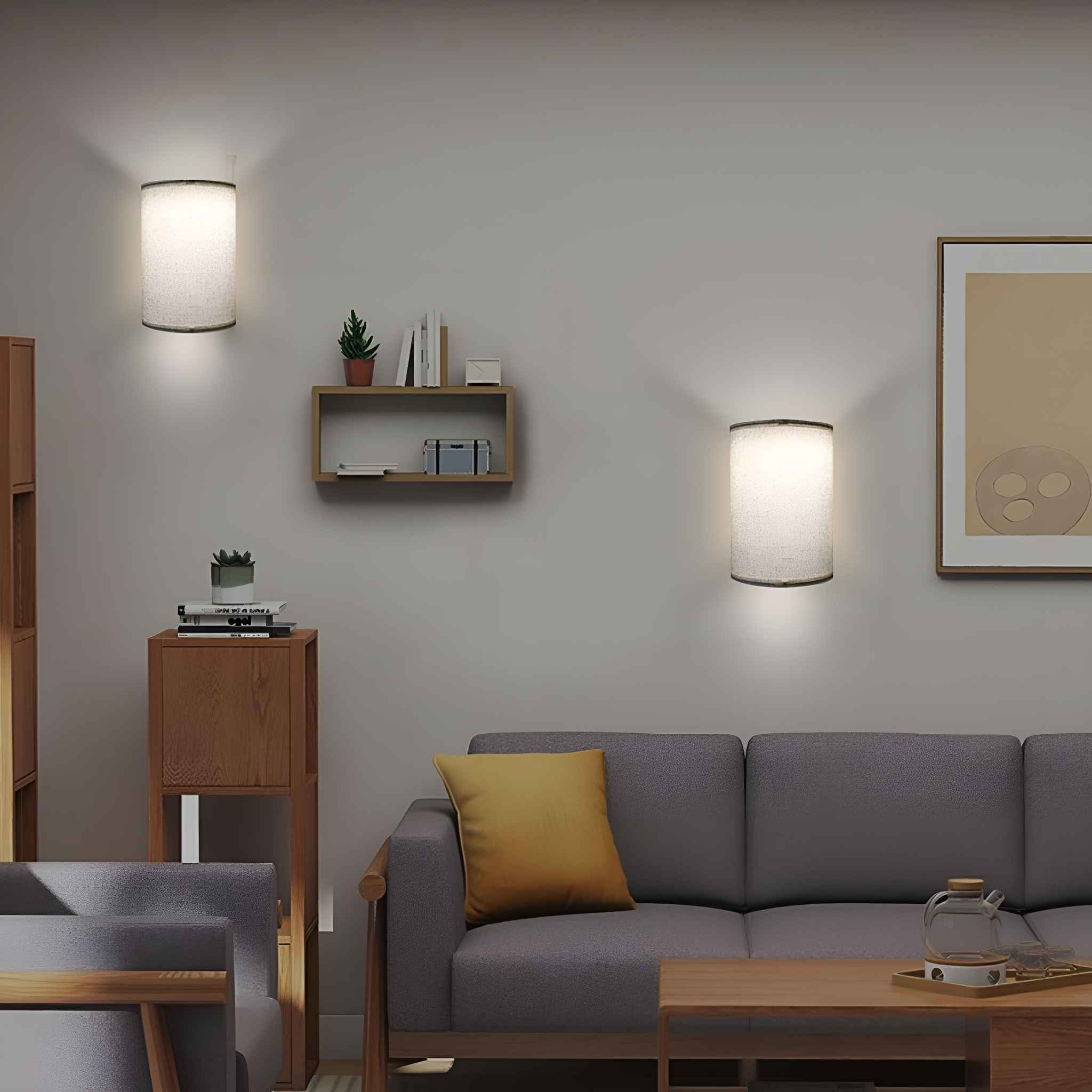 Ein Wohnzimmer mit zwei Wandlampen, einem Sofa, Holzmöbeln und einem gerahmten Bild an einer hellgrauen Wand.