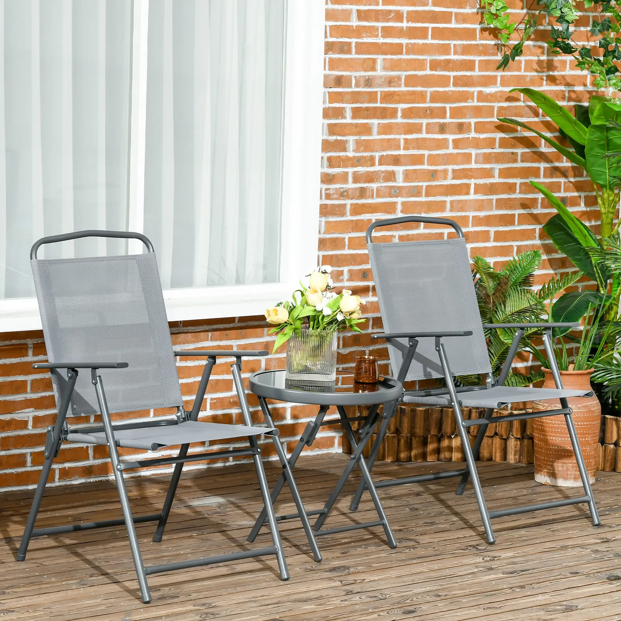 Szene im Freien: 2 Stühle, ein Tisch, Blumen, eine Backsteinmauer und Pflanzen.
