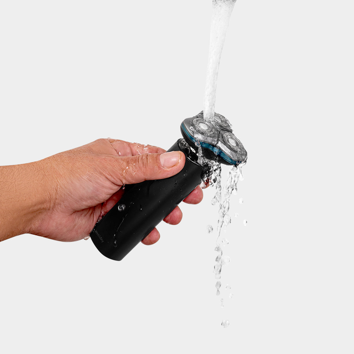 Mano sosteniendo una afeitadora eléctrica negra bajo agua corriente.