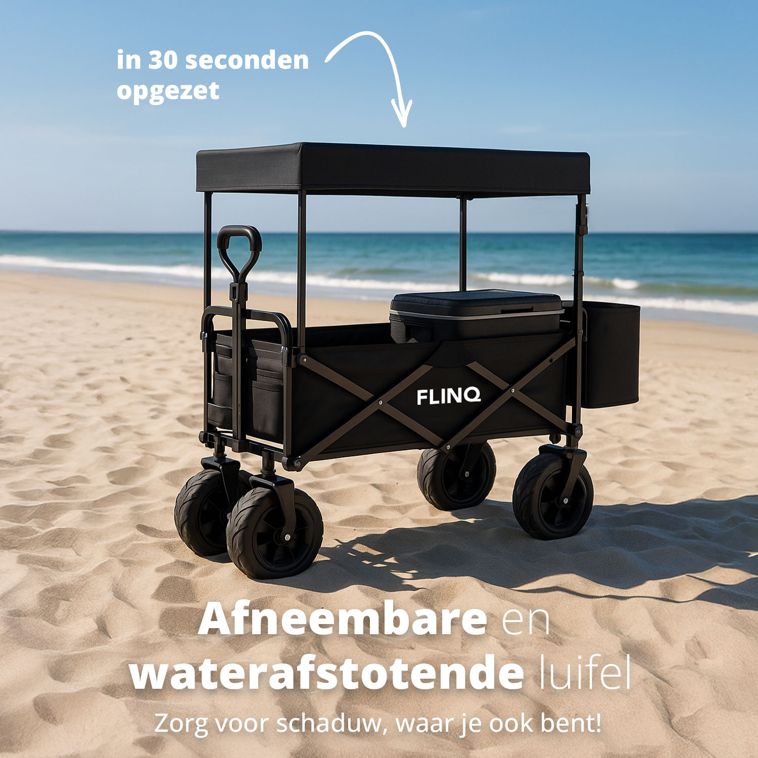 Un chariot pliant noir avec un auvent amovible sur une plage de sable avec l'océan en arrière-plan.