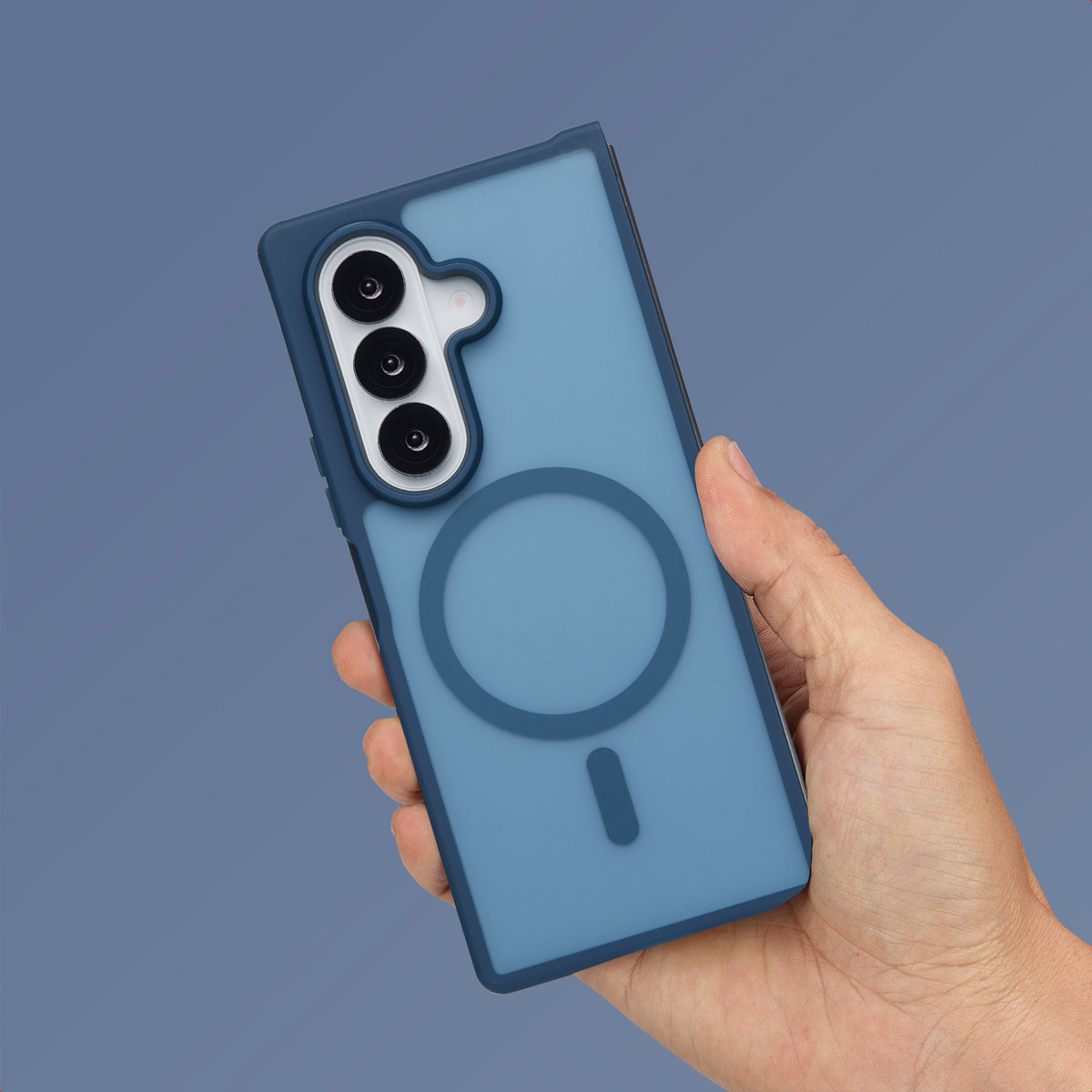 Een hand die een blauwe telefoonhoes vasthoudt met een cirkelvormige MagSafe-ring en drie cameralenzen.
