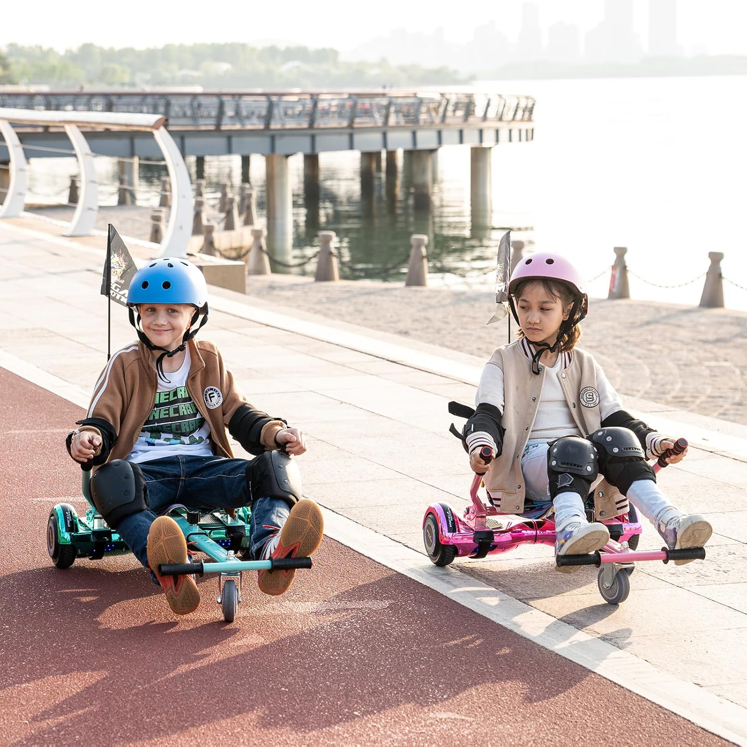 Dos niños en karts en un camino pavimentado cerca del agua. Uno usa casco azul, el otro rosa.