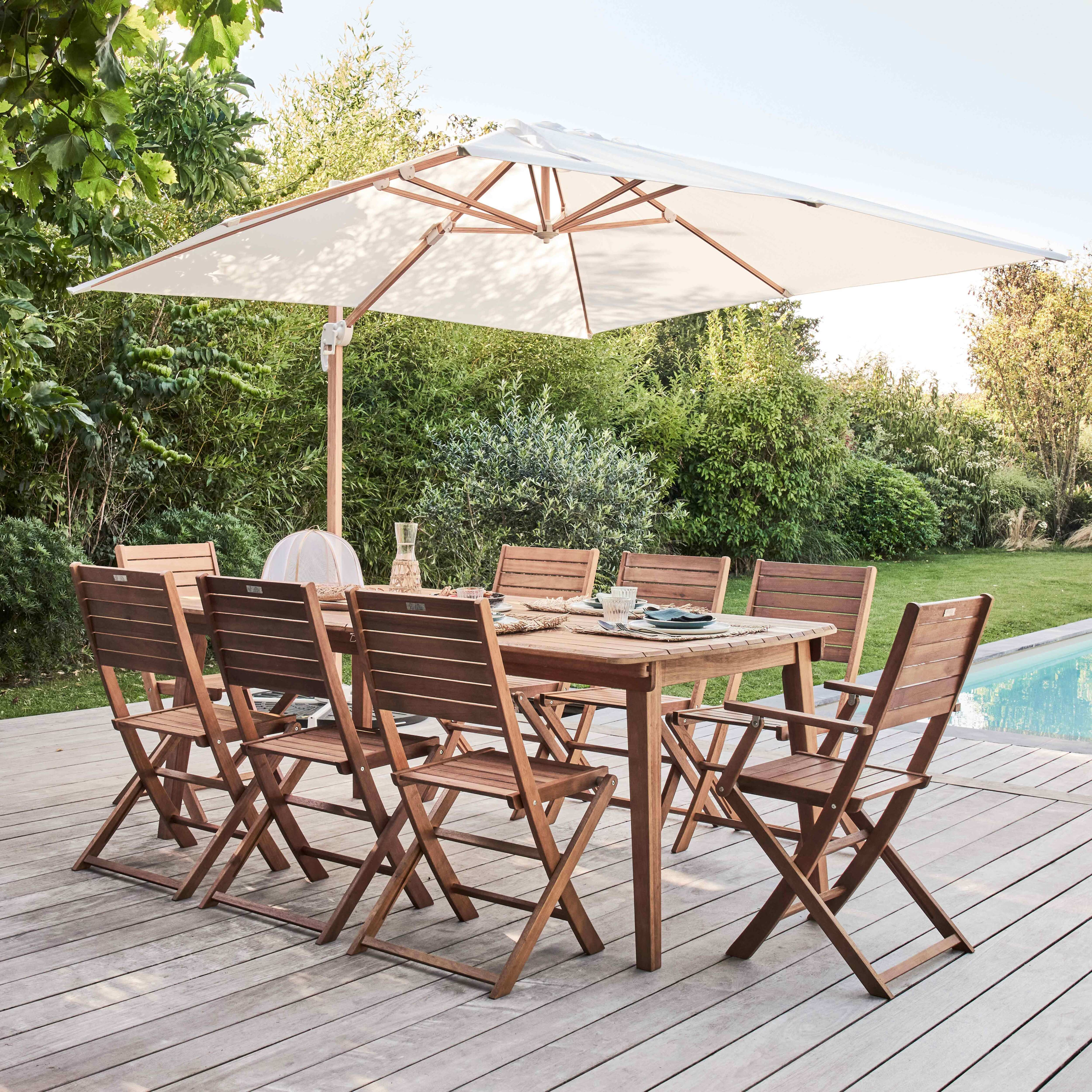Holzterrassenset mit Tisch, Stühlen und großem Schirm. Grünes Laub im Hintergrund.