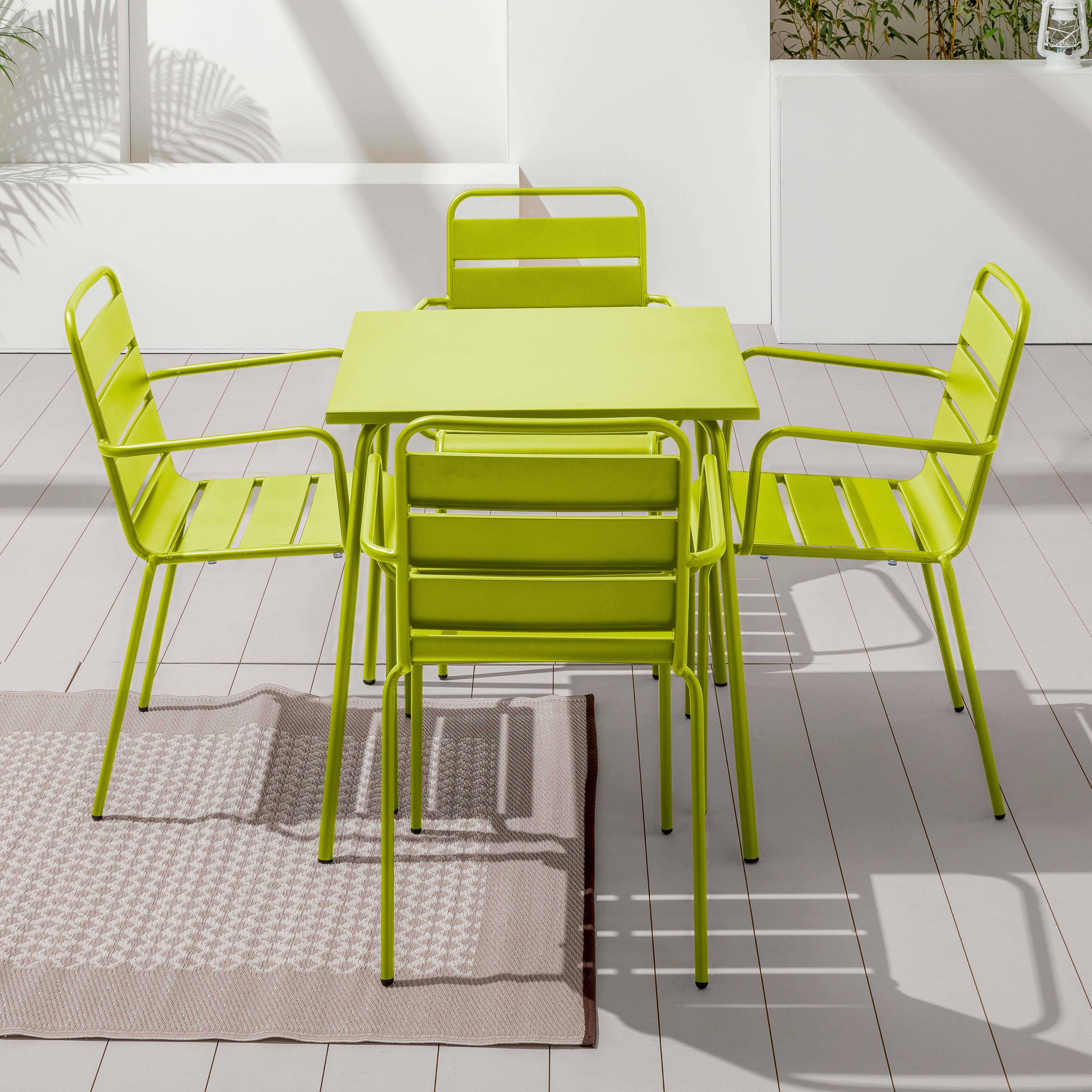 Ein limettengrüner Metalltisch und Stühle stehen auf einer Terrasse mit einem gemusterten Teppich.