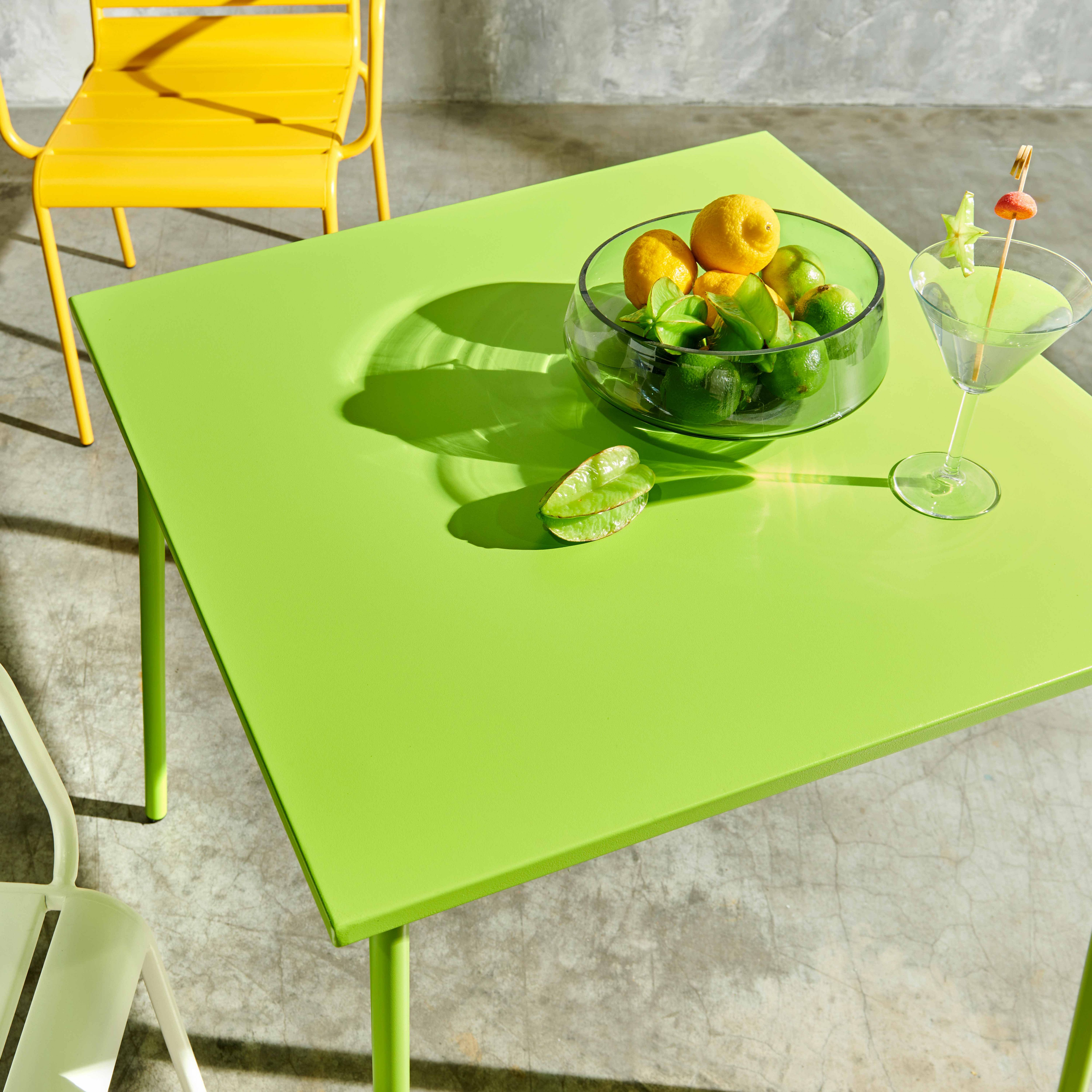 Ein grüner quadratischer Tisch mit einer Schüssel Limetten und Zitronen und einem Cocktail.