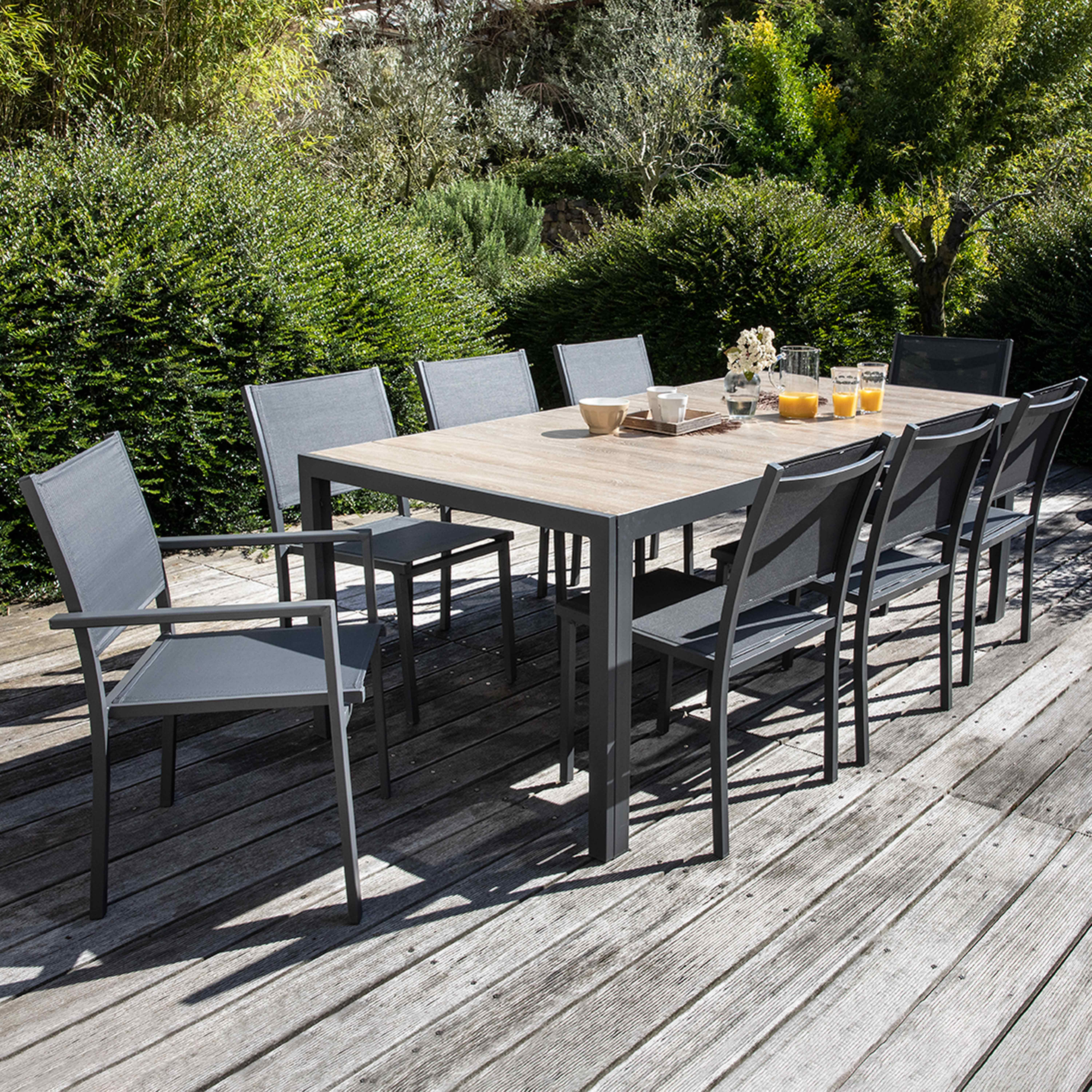 Eine Holzterrasse mit einem Tisch und Stühlen im Freien. Grüne Büsche im Hintergrund.