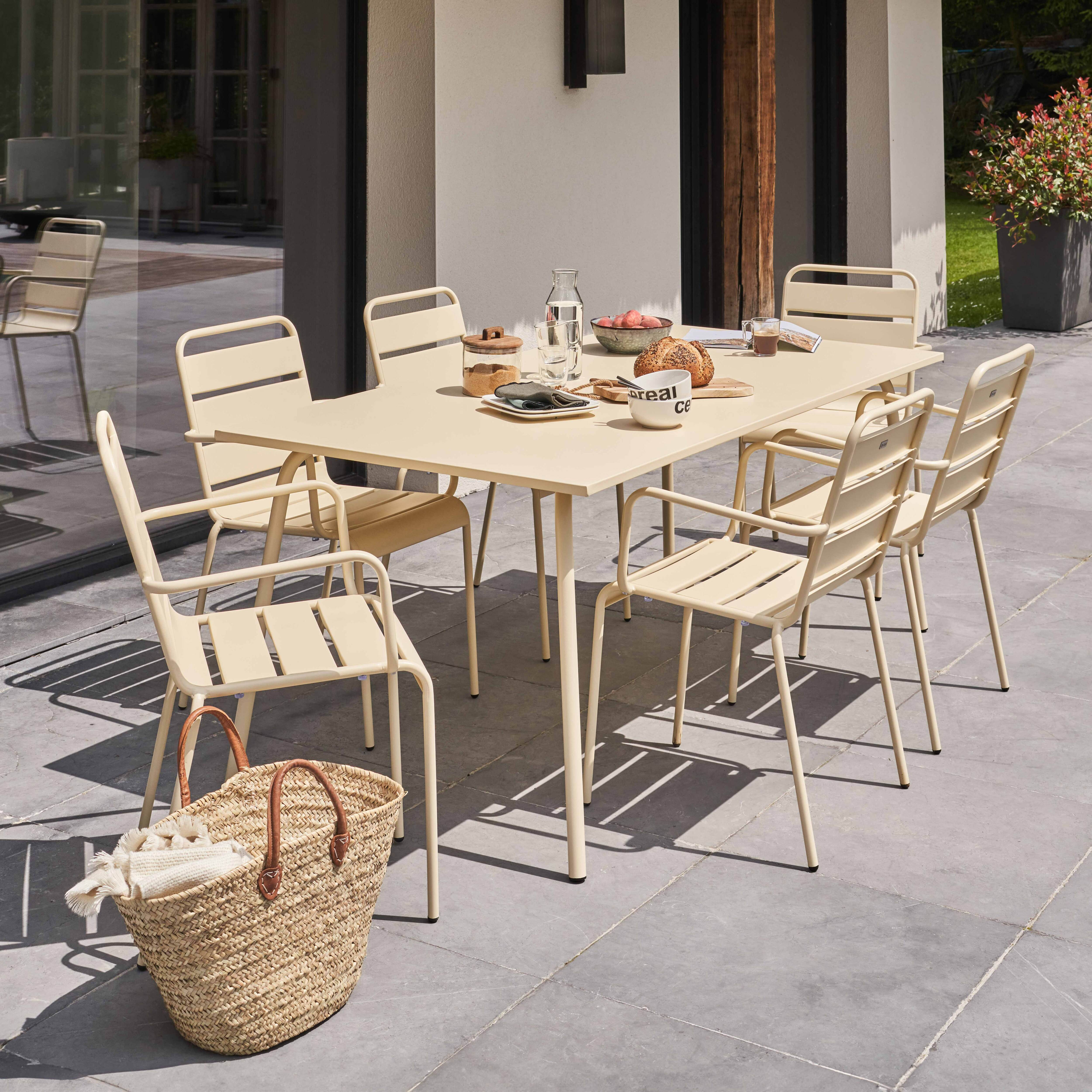 Ein Essbereich im Freien mit einem beigen Tisch, Stühlen und einem gewebten Korb auf einer grauen Terrasse.