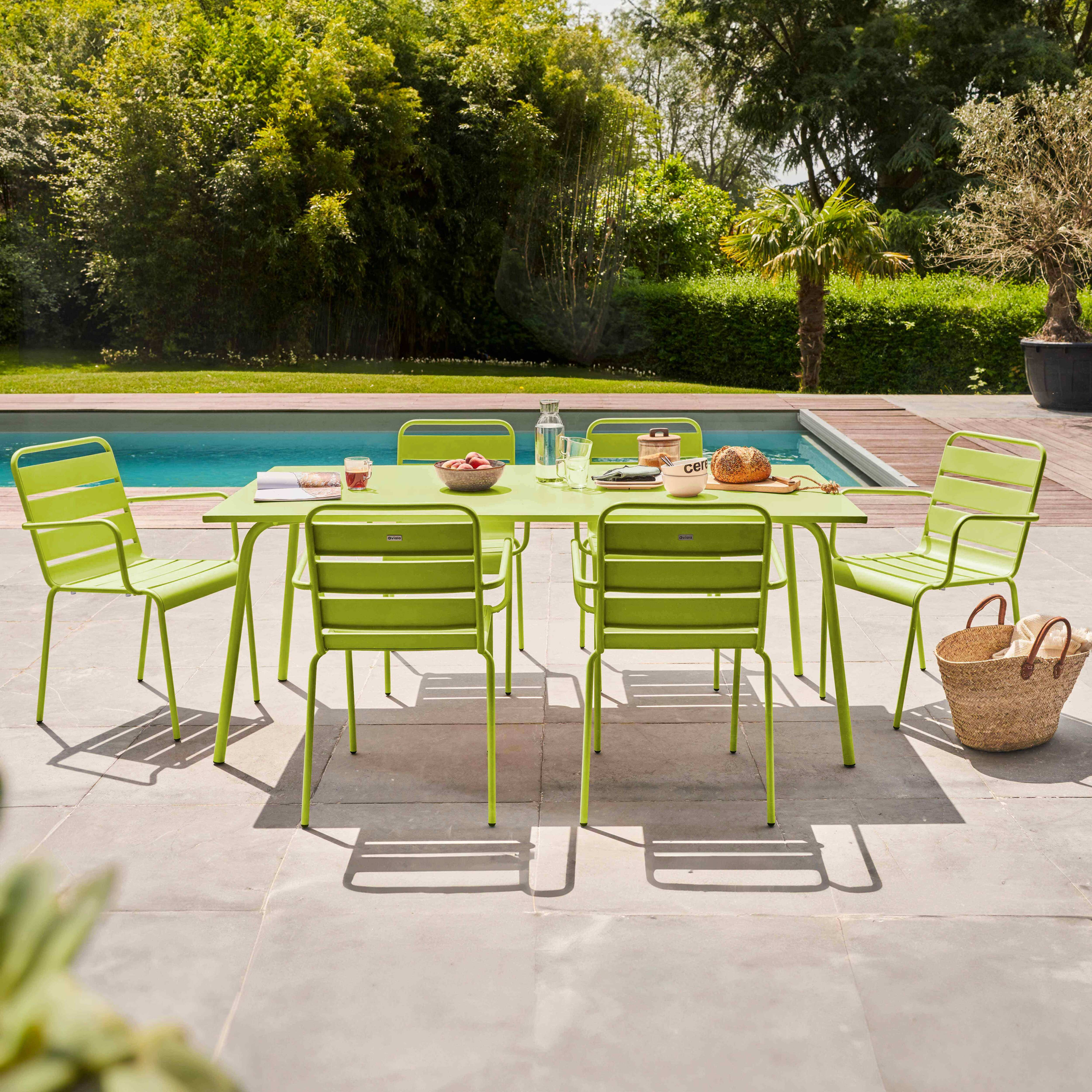 Outdoor-Essgruppe mit grünem Metalltisch und Stühlen am Pool, umgeben von üppigem Grün.