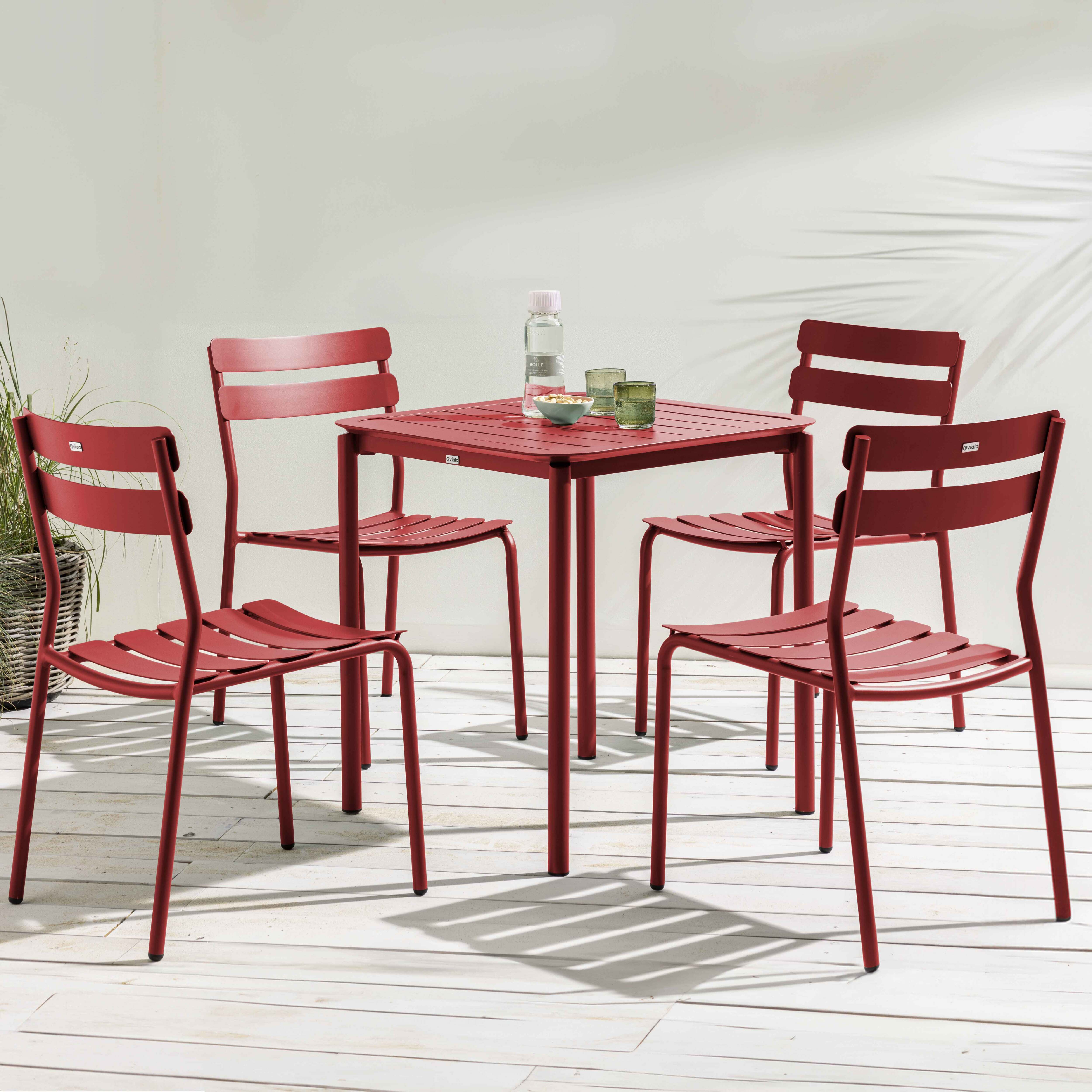 Ein Tisch mit vier Stühlen, rot. Draußen aufgestellt, mit Pflanzen im Hintergrund.