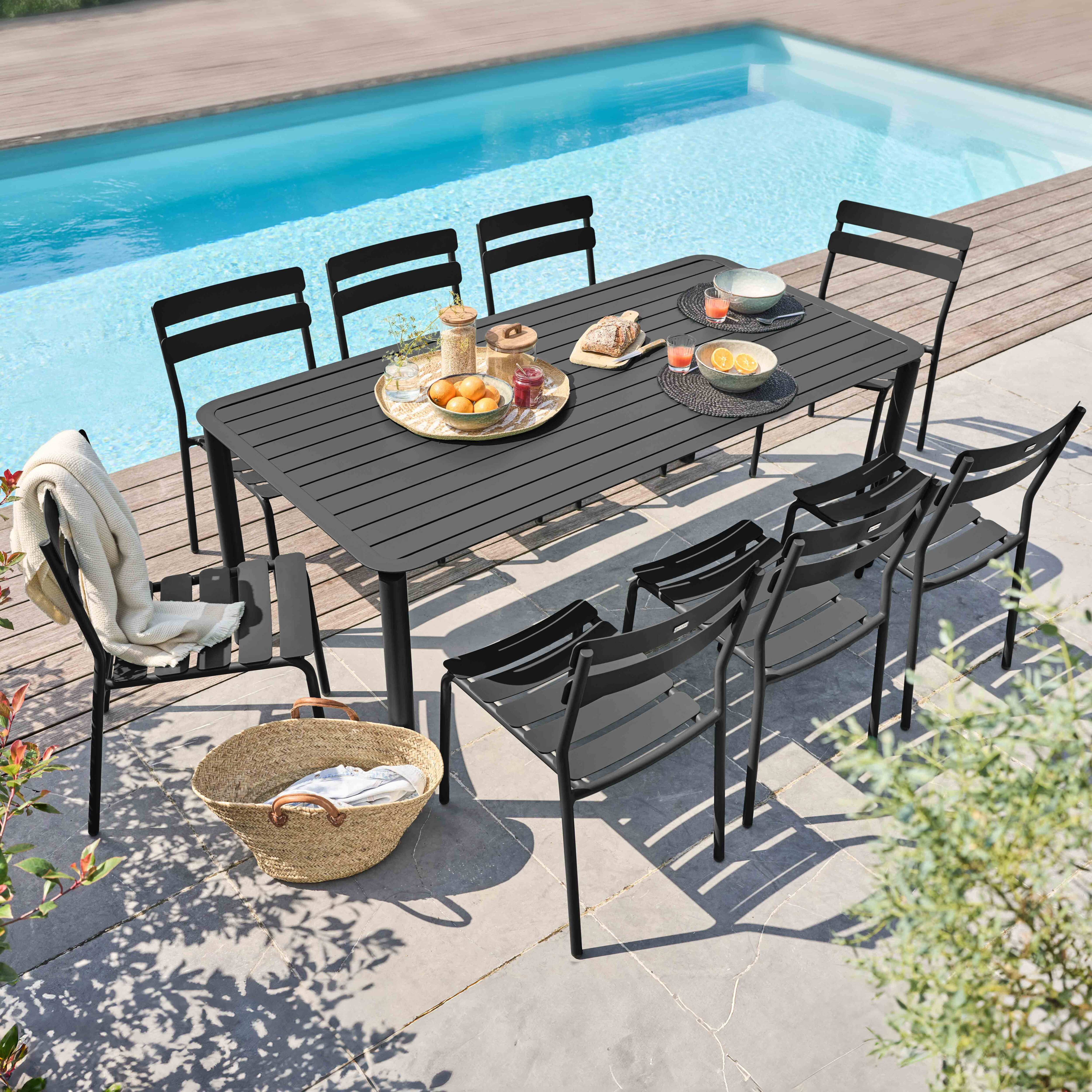 Ess-Set mit schwarzem Tisch und Stühlen neben einem Pool. Essen und Getränke auf dem Tisch.