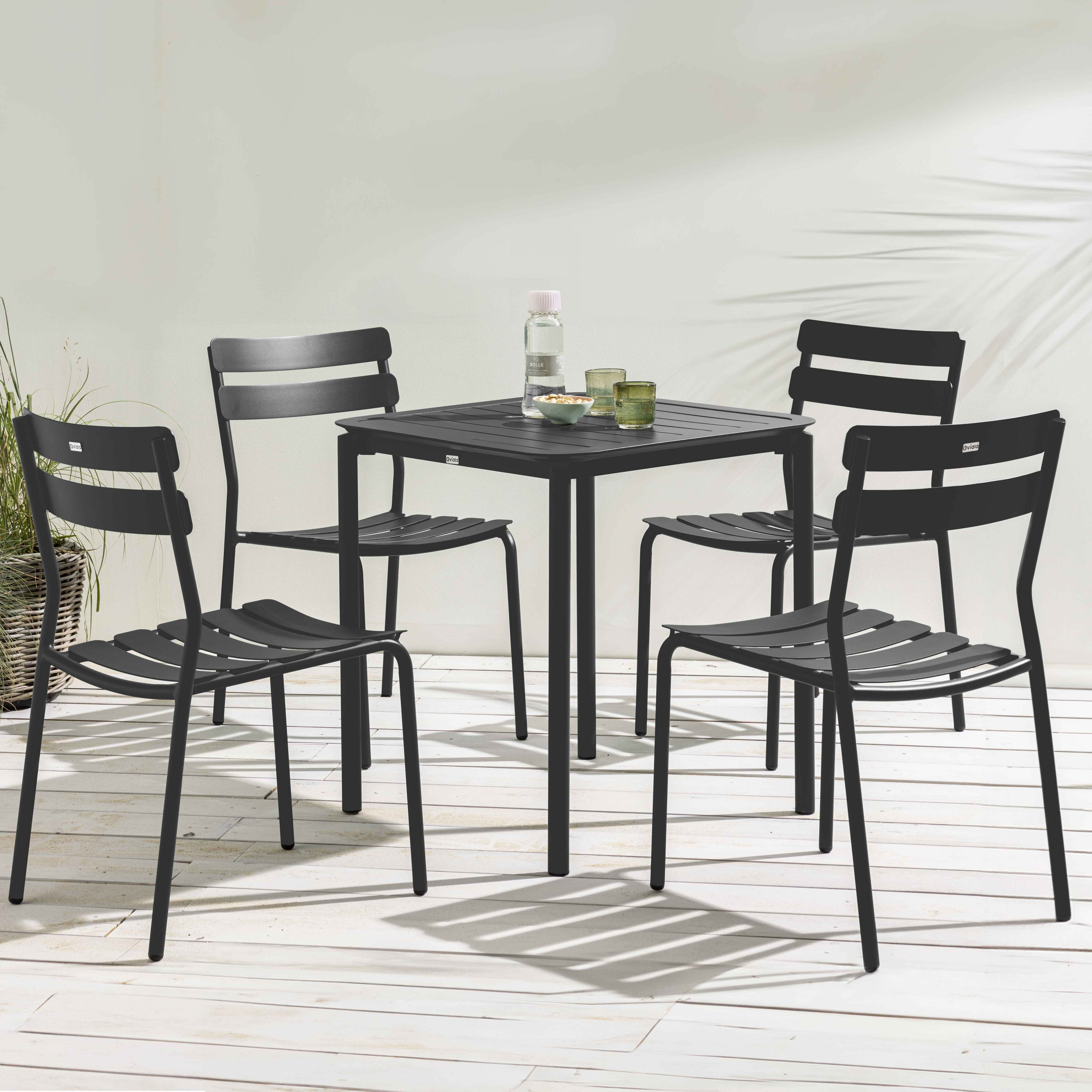 Ein schwarzer Tisch und vier Stühle sind auf einer weißen Terrasse mit einigen Getränken auf dem Tisch angeordnet.