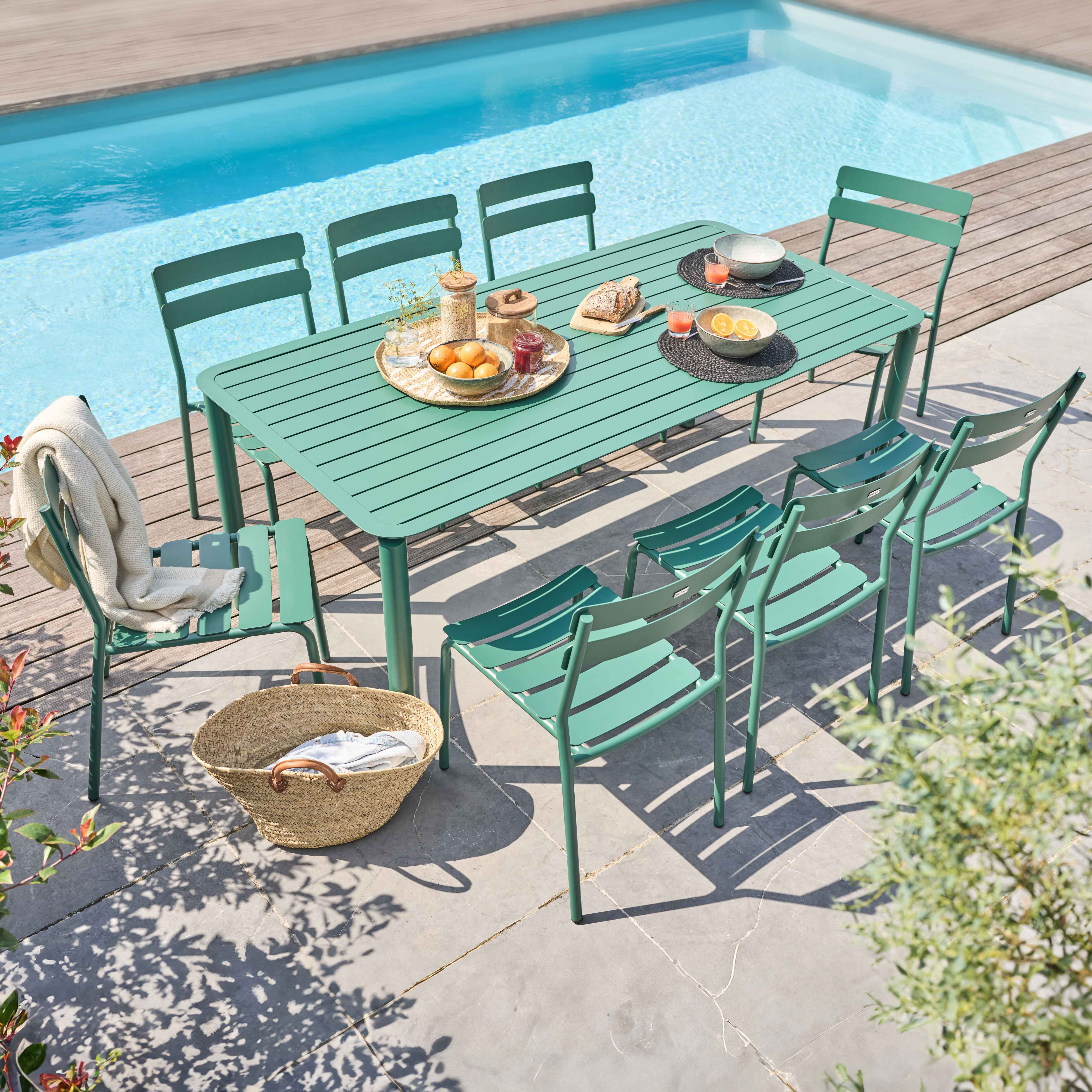 Grüner Tisch und Stühle am Pool. Korb, Essen und Getränke auf dem Tisch. Blauer Pool, Holzdeck.