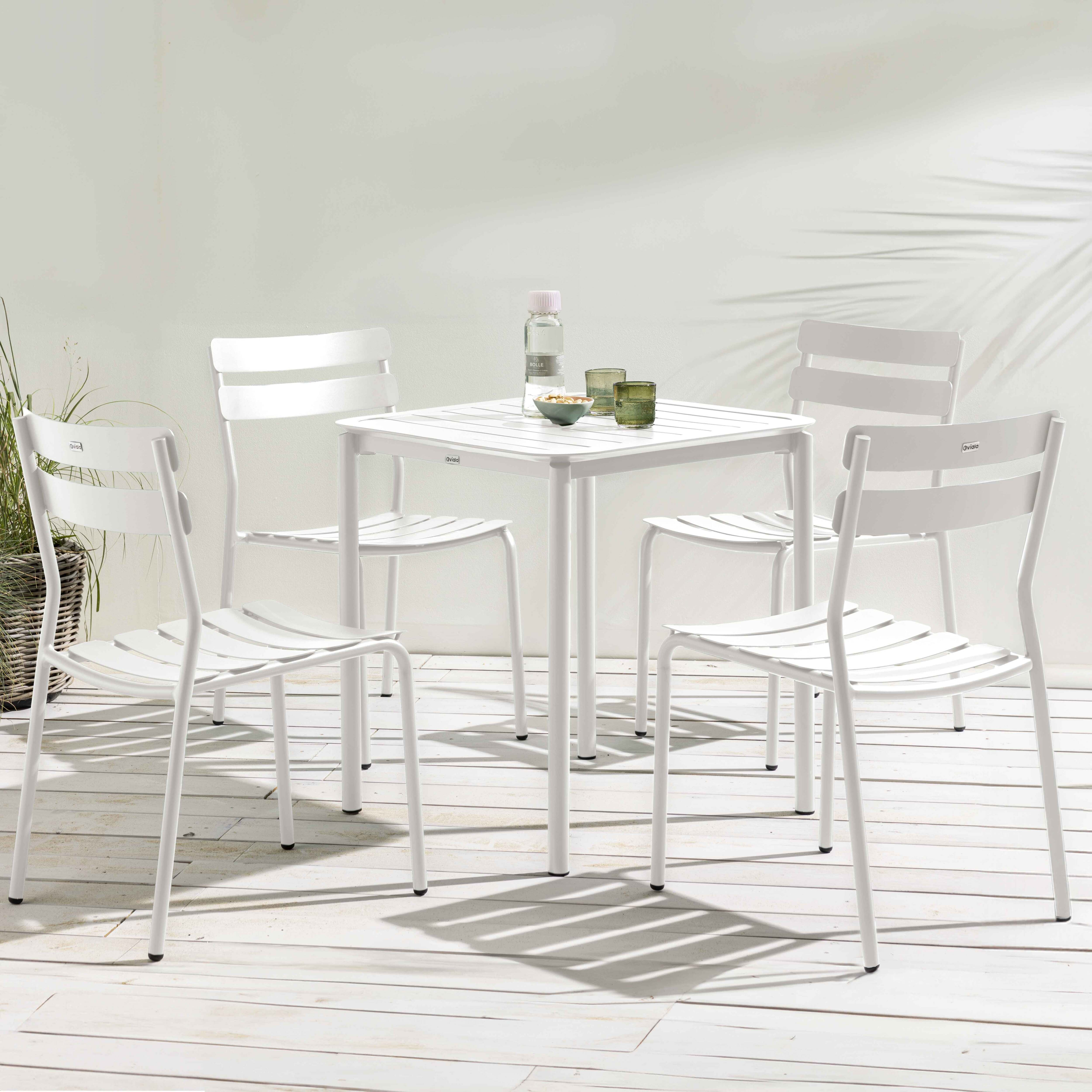 Outdoor-Szene mit einem weißen quadratischen Tisch und vier passenden Stühlen auf einer hellen Holzterrasse.