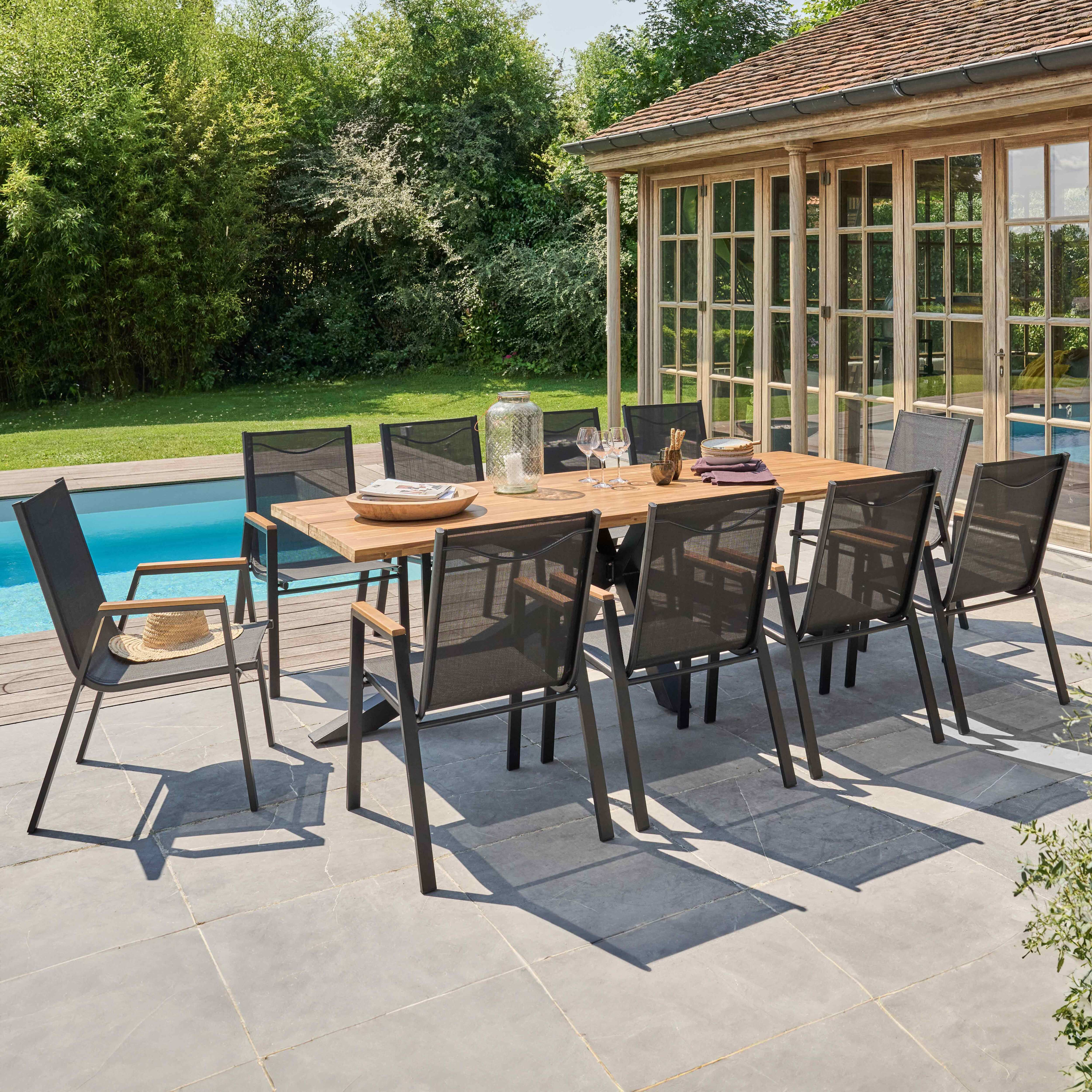 Outdoor-Essgruppe mit Holztisch und grauen Metallstühlen, umgeben von üppigem Grün.