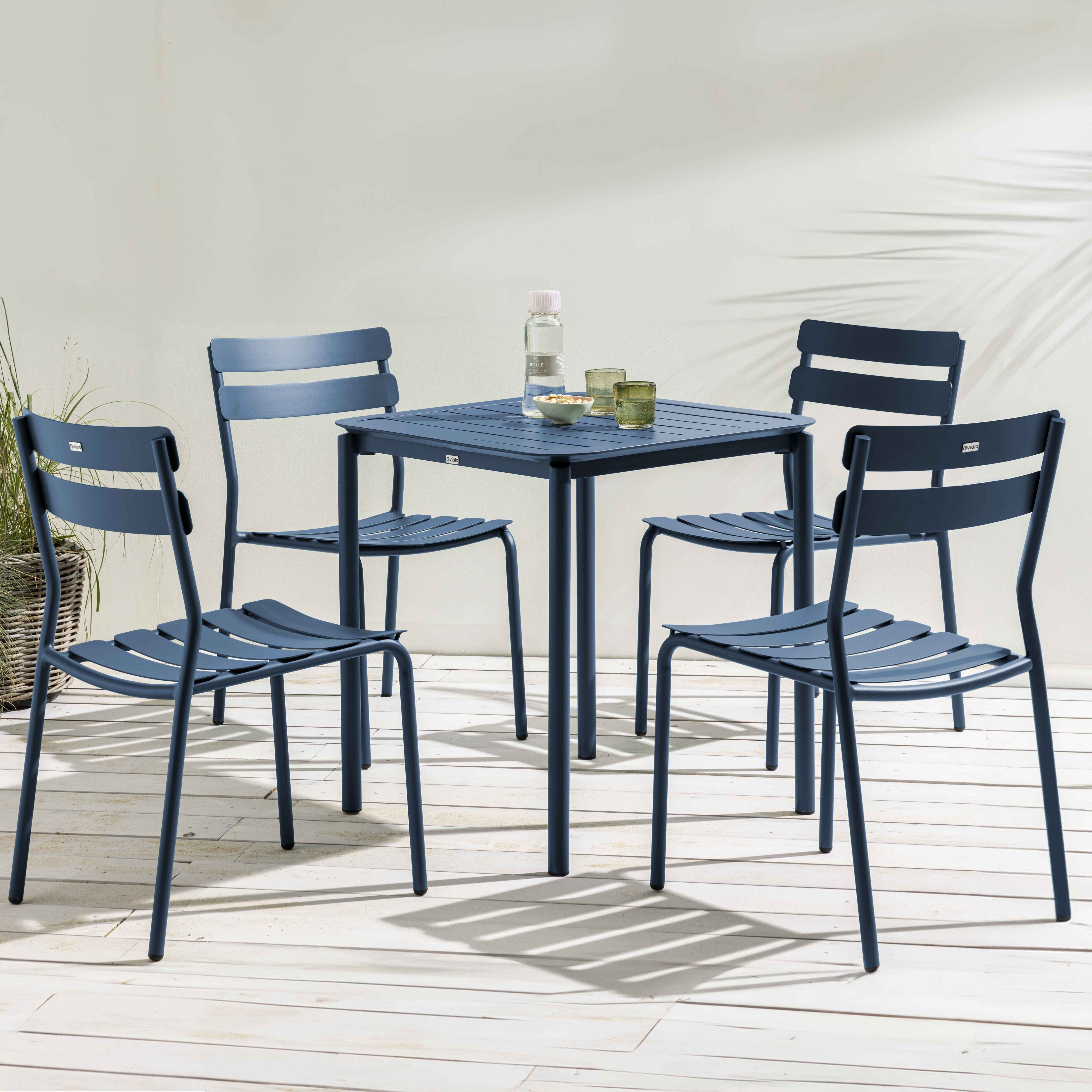 Ein blaues Ess-Set im Freien mit einem quadratischen Tisch und vier Stühlen auf einem Holzdeck.