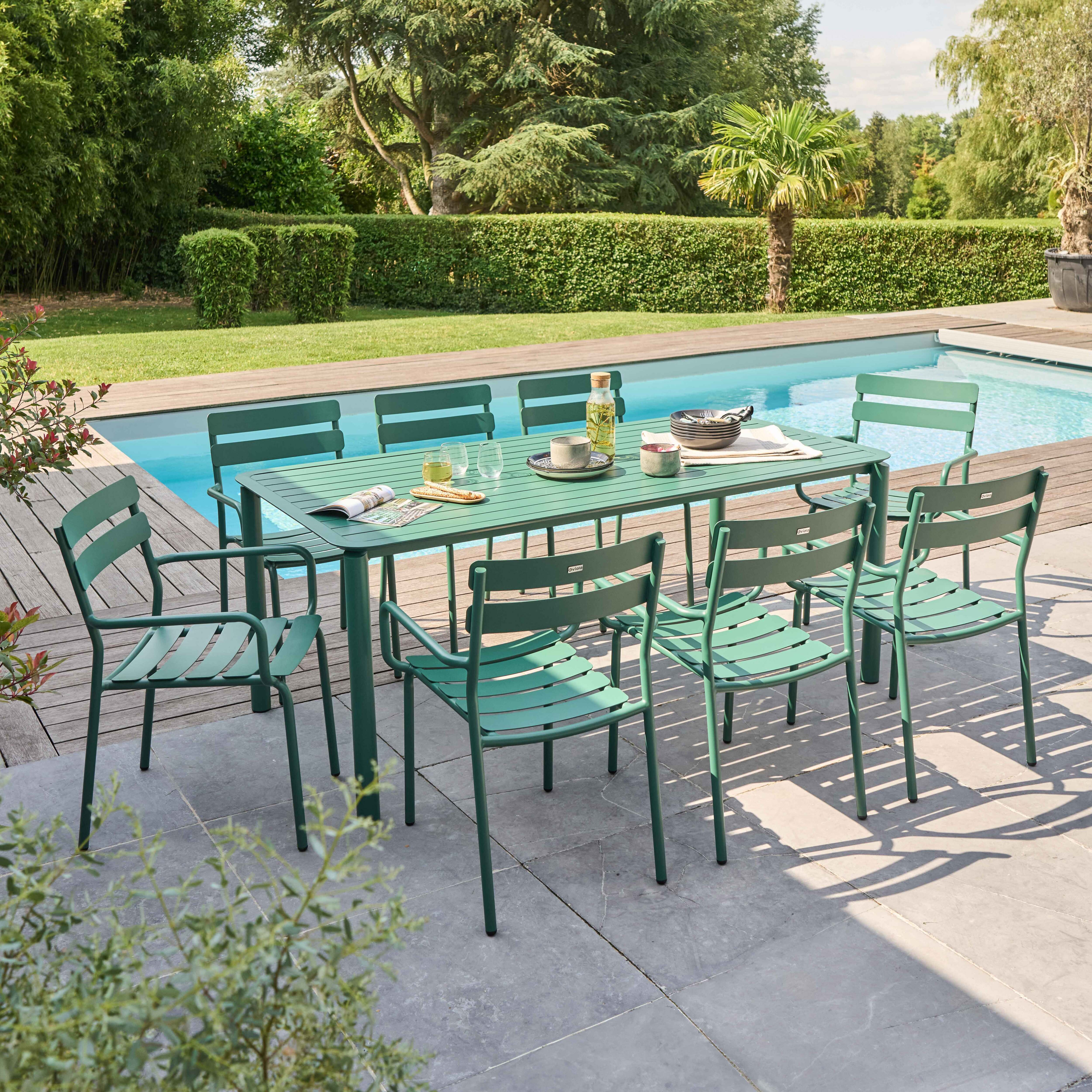 Ein grünes Ess-Set für draußen mit Tisch und Stühlen in der Nähe eines Pools.