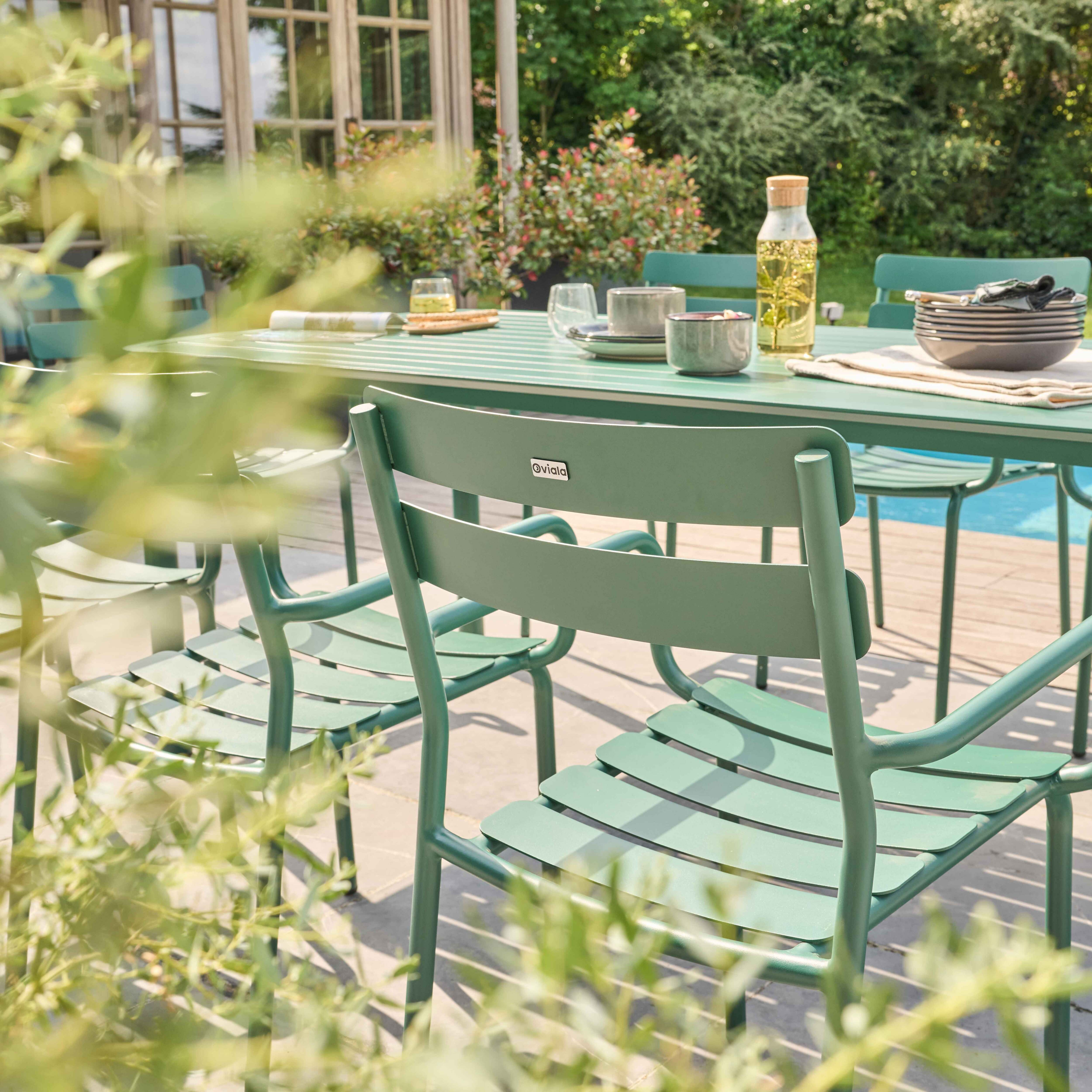 Ein grüner Tisch und Stühle in einem Garten, mit verschwommenem Hintergrund aus Grün und einem Haus.