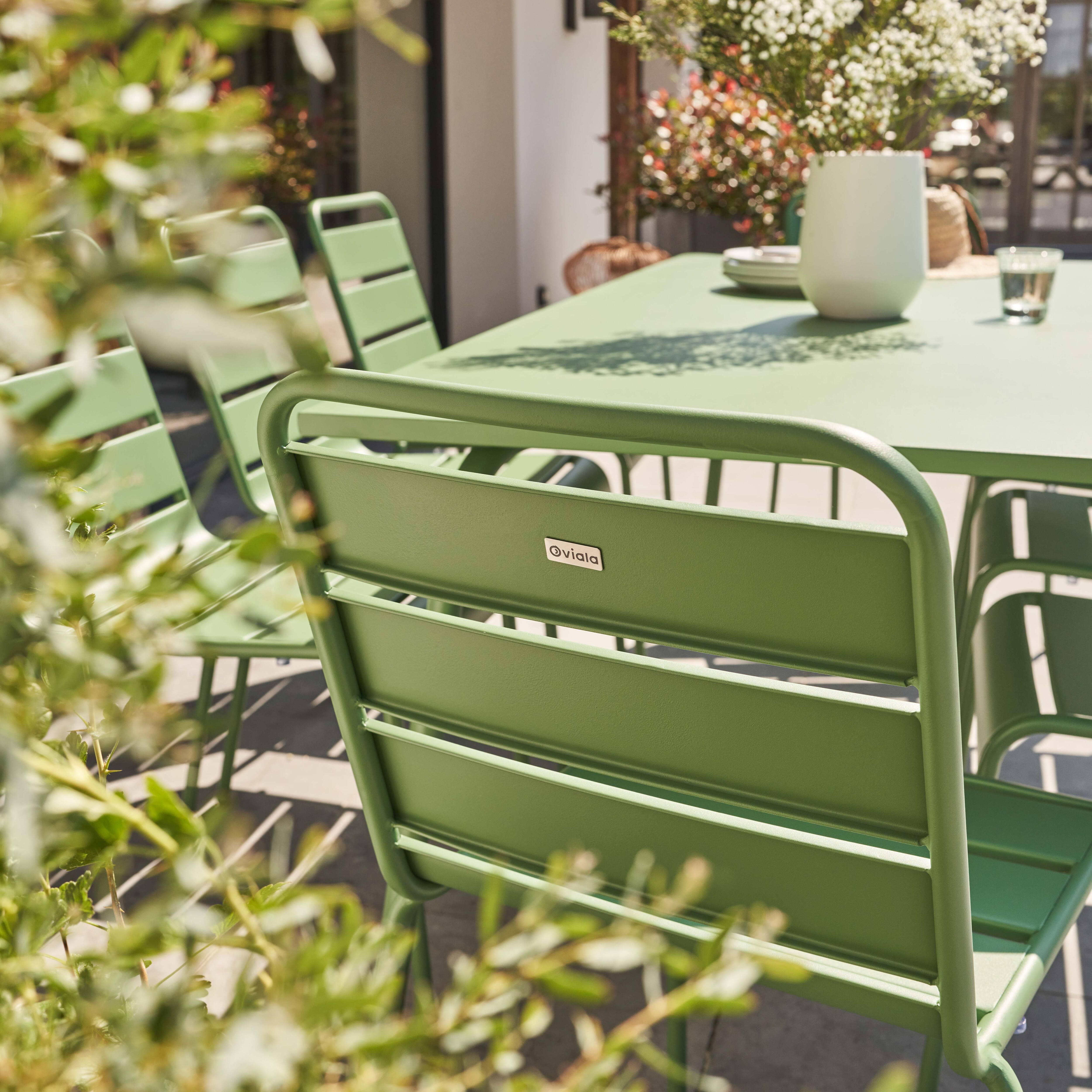 Grüne Stühle und Tisch in einem Garten, umgeben von grünem Laub.