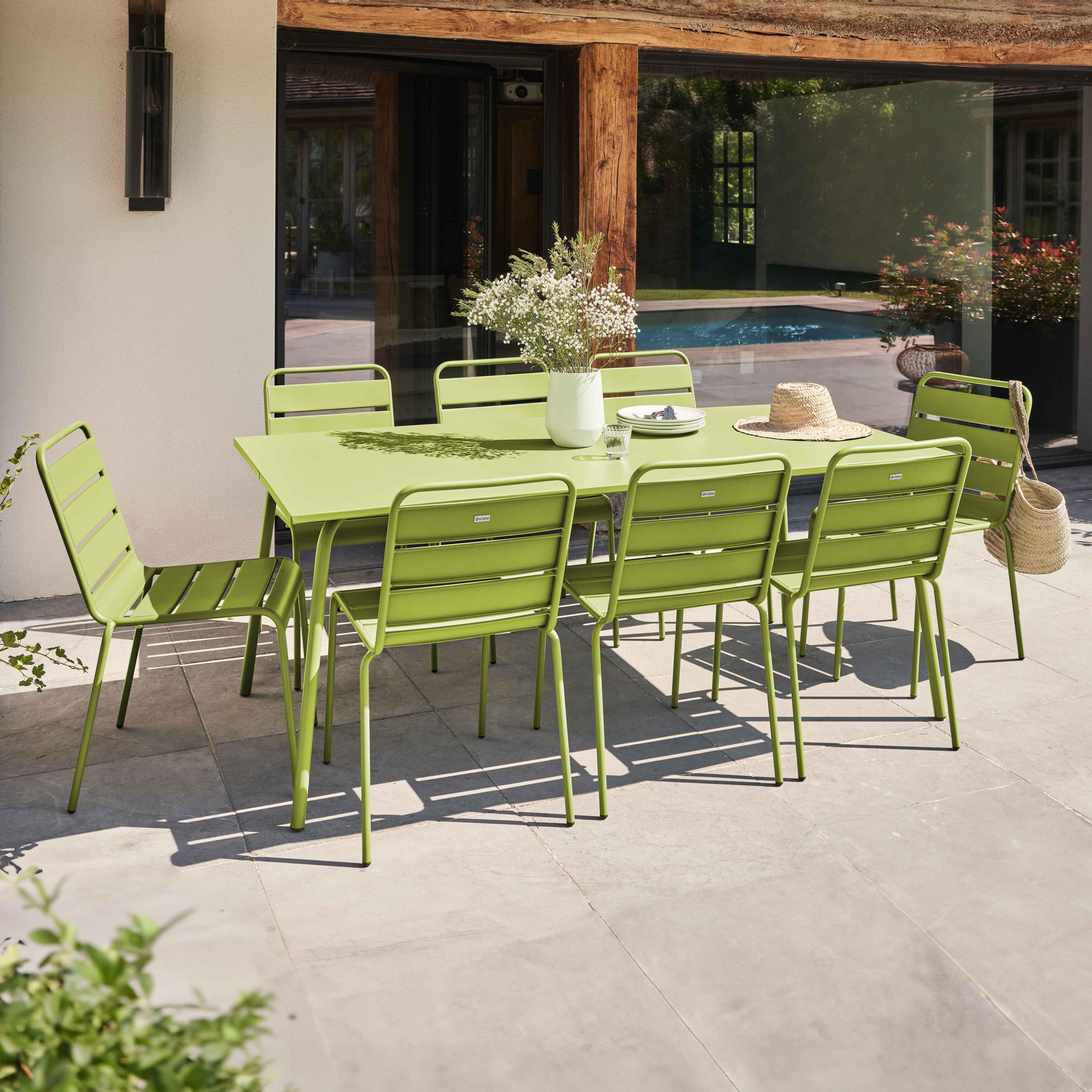 Ein grüner Metalltisch und Stühle auf einer Terrasse im Freien, mit einem Haus und Garten im Hintergrund.