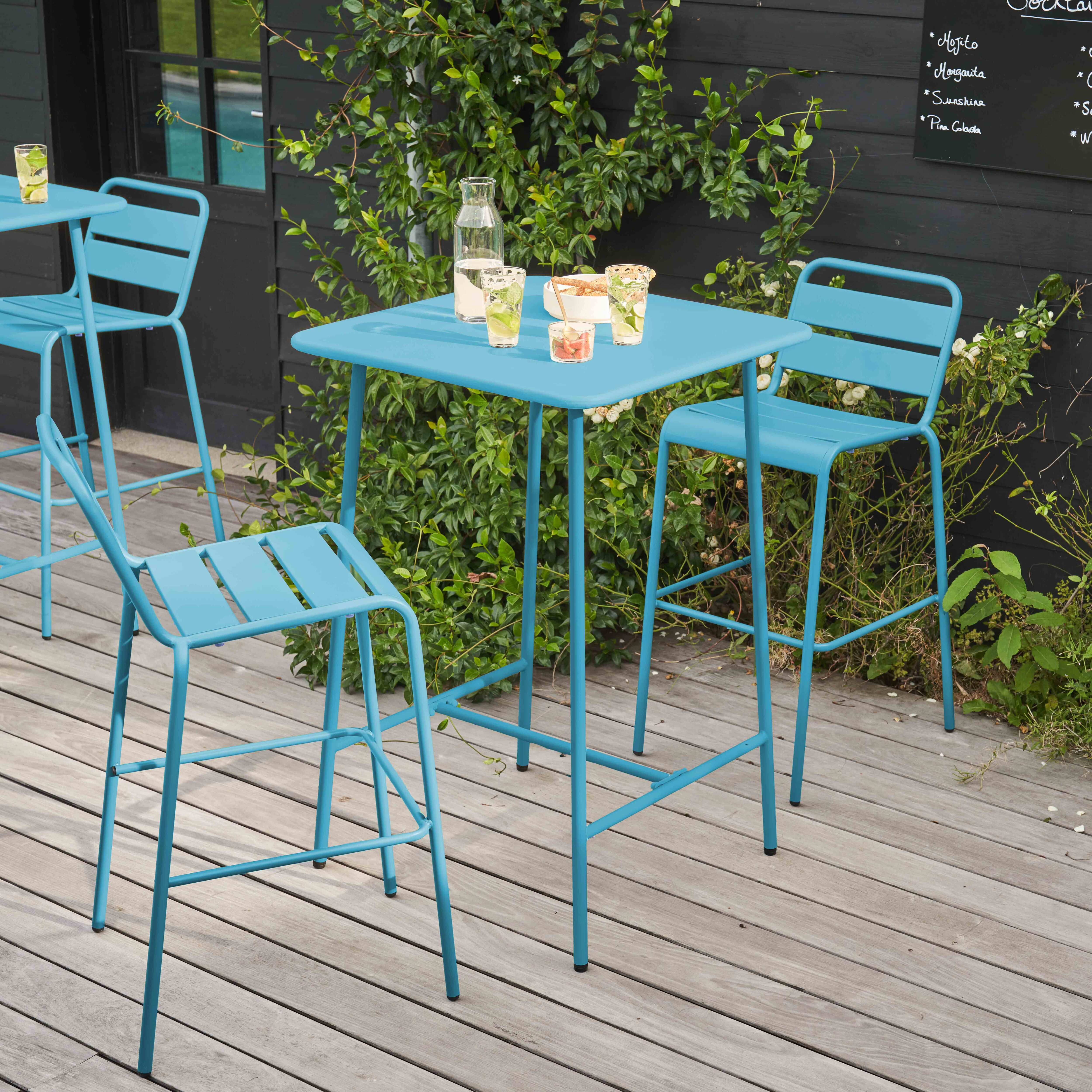 Ein blauer Metalltisch und Stühle auf einer Holzterrasse, mit Getränken und Snacks auf dem Tisch.