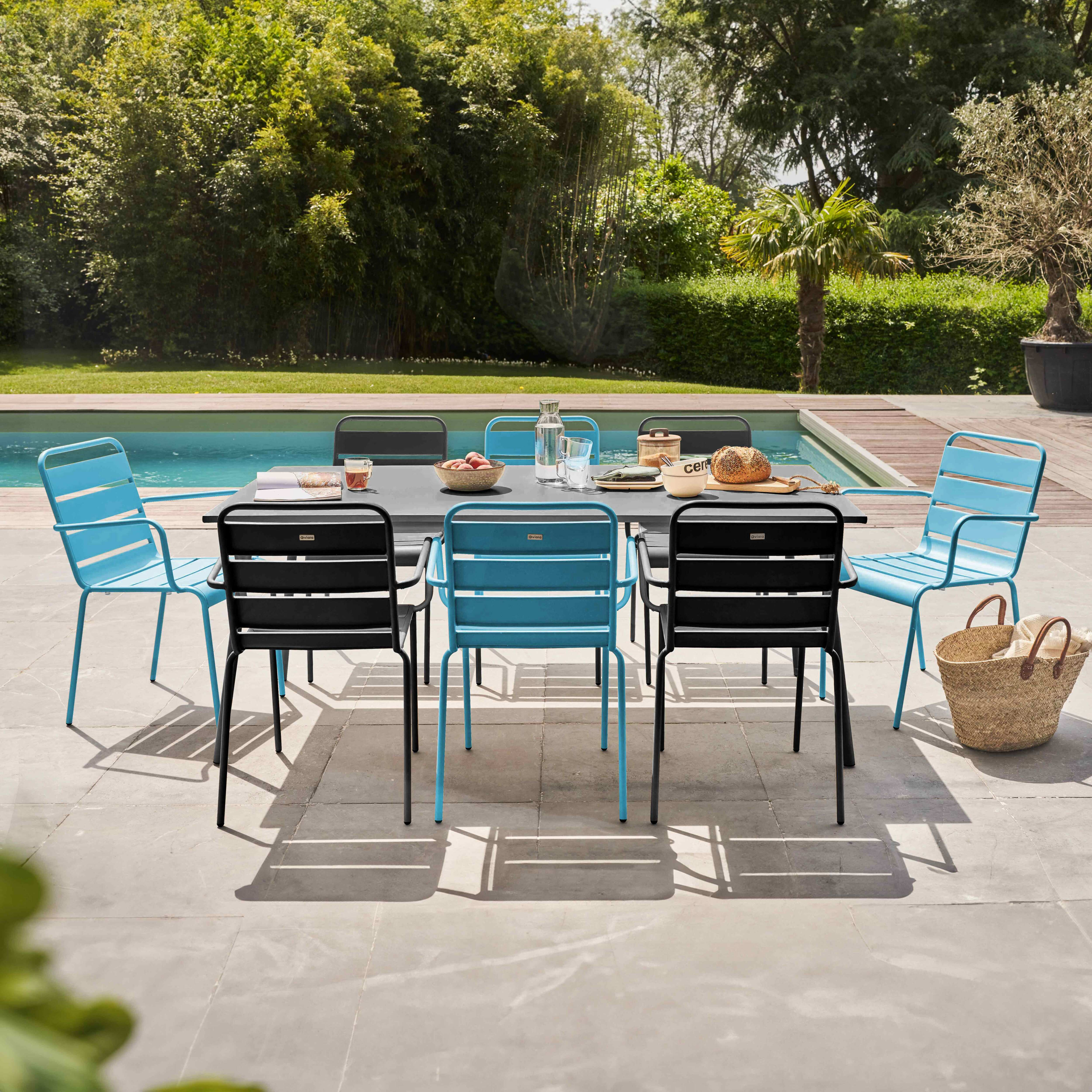 Outdoor-Essgruppe mit grauem Tisch, blauen und schwarzen Stühlen und einem Pool im Hintergrund.