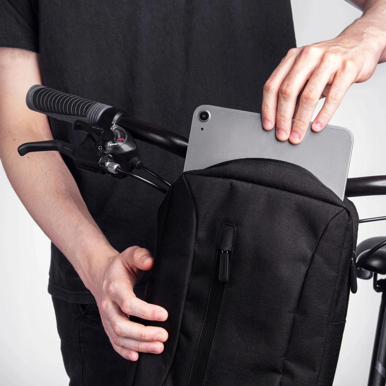 Osoba trzymająca tablet w torbie rowerowej, widoczna kierownica roweru i czarna torba.